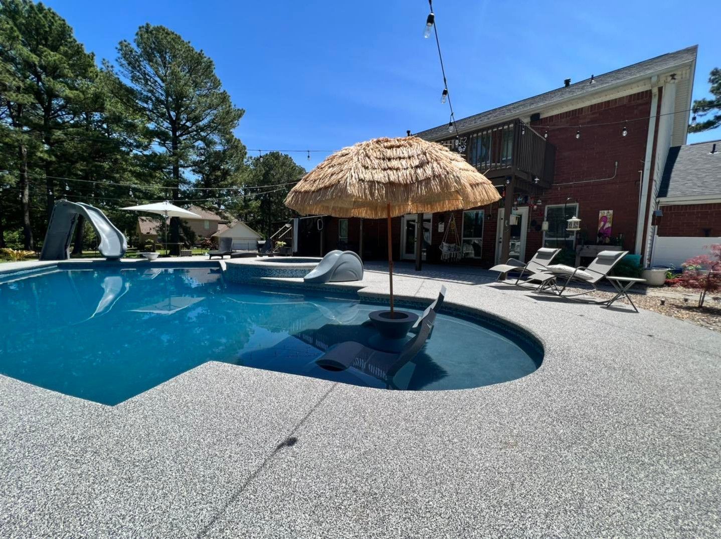 A large swimming pool with a thatched umbrella in the middle of it.