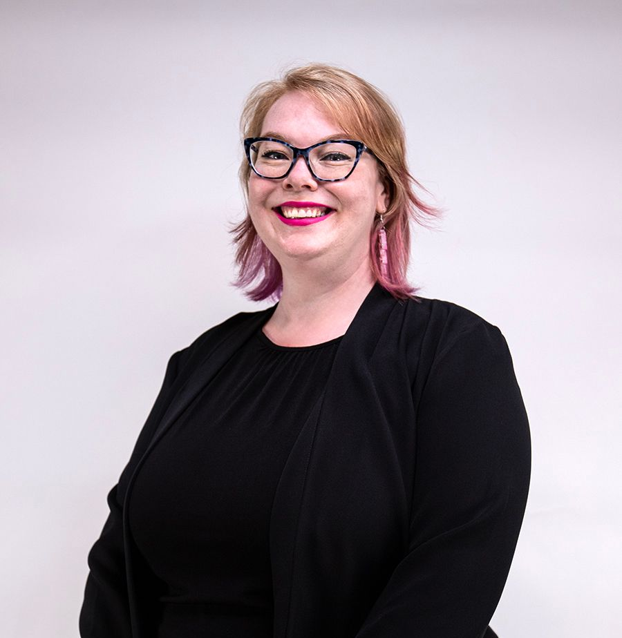 Woman in a pink blazer smiles at the camera, studio shot.