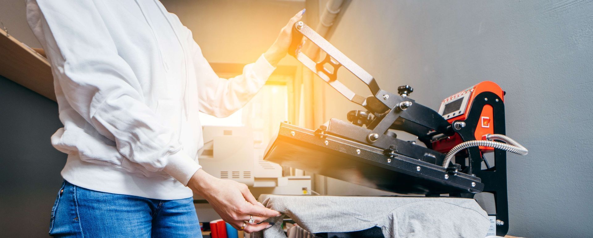 Person using a screen printing machine to apply a design to a t-shirt in a workshop.