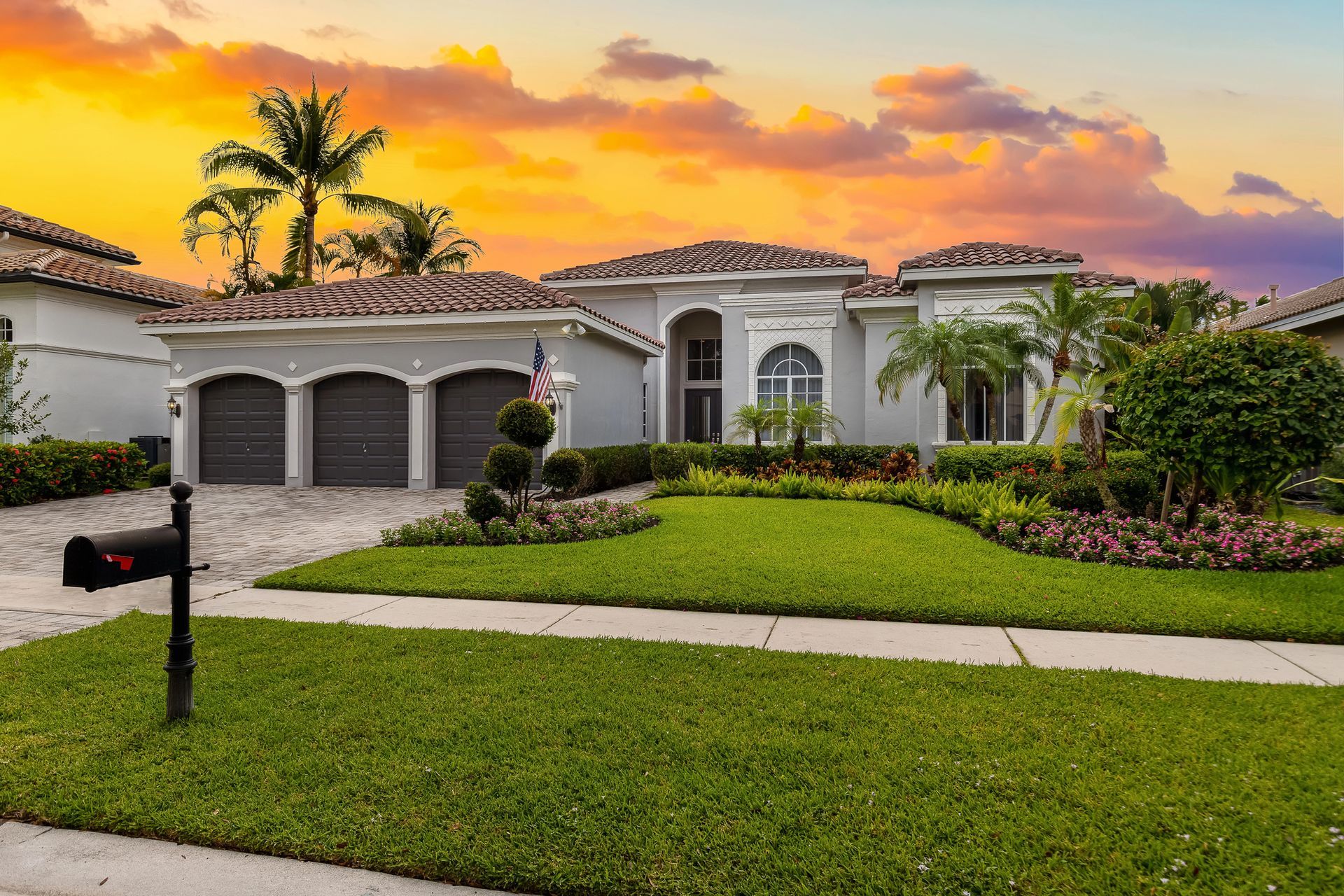Sunset view of a white stucco home with a tiled roof, palm trees, and a manicured front lawn