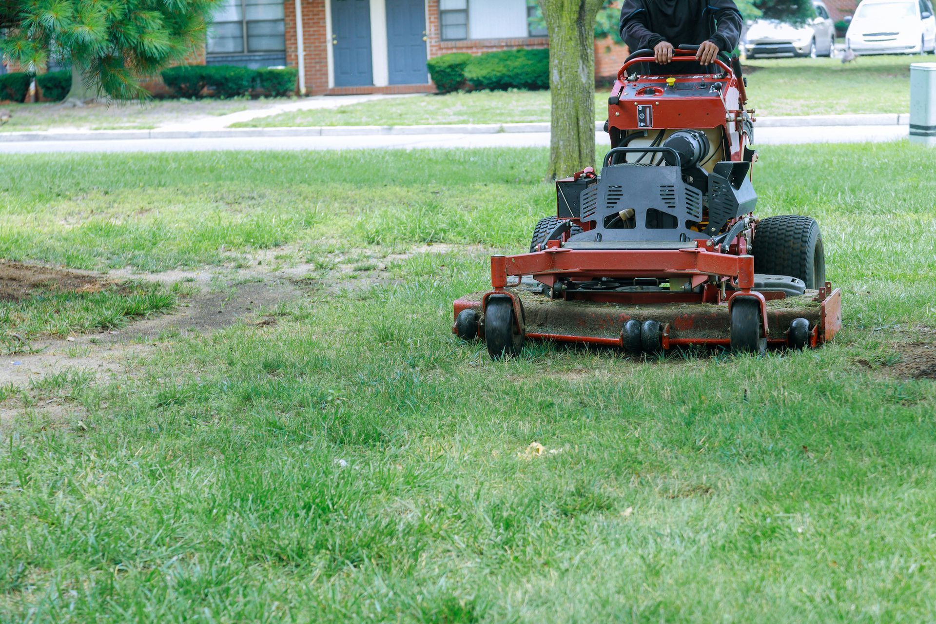 A person on a red zero-turn mower cutting grass on a residential lawn.