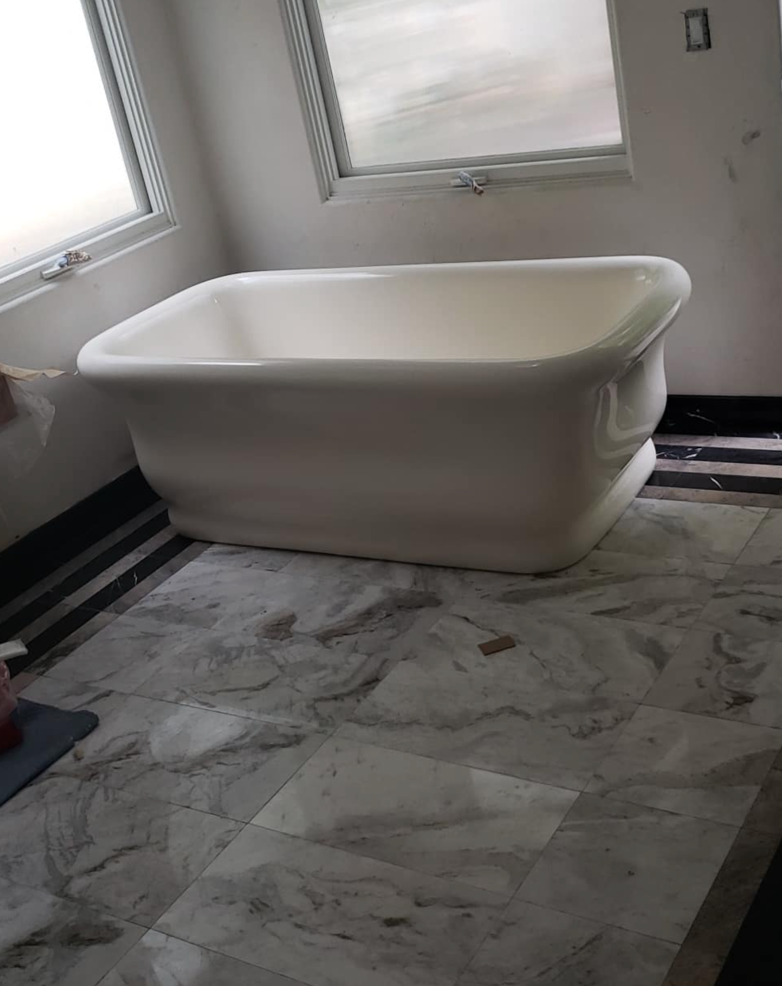 A white bathtub is sitting on a marble floor in a bathroom.