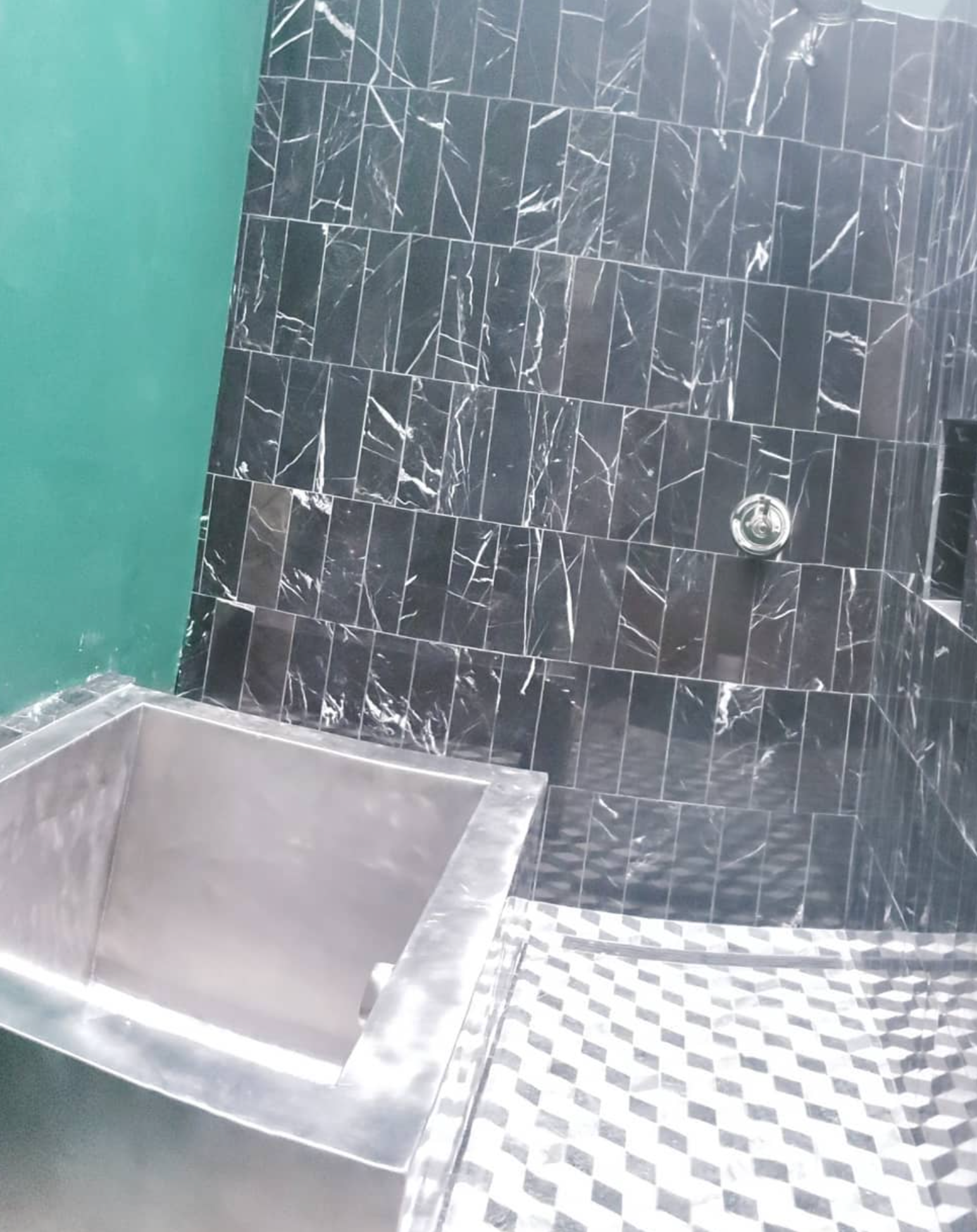 A bathroom with black tiles and a stainless steel tub.
