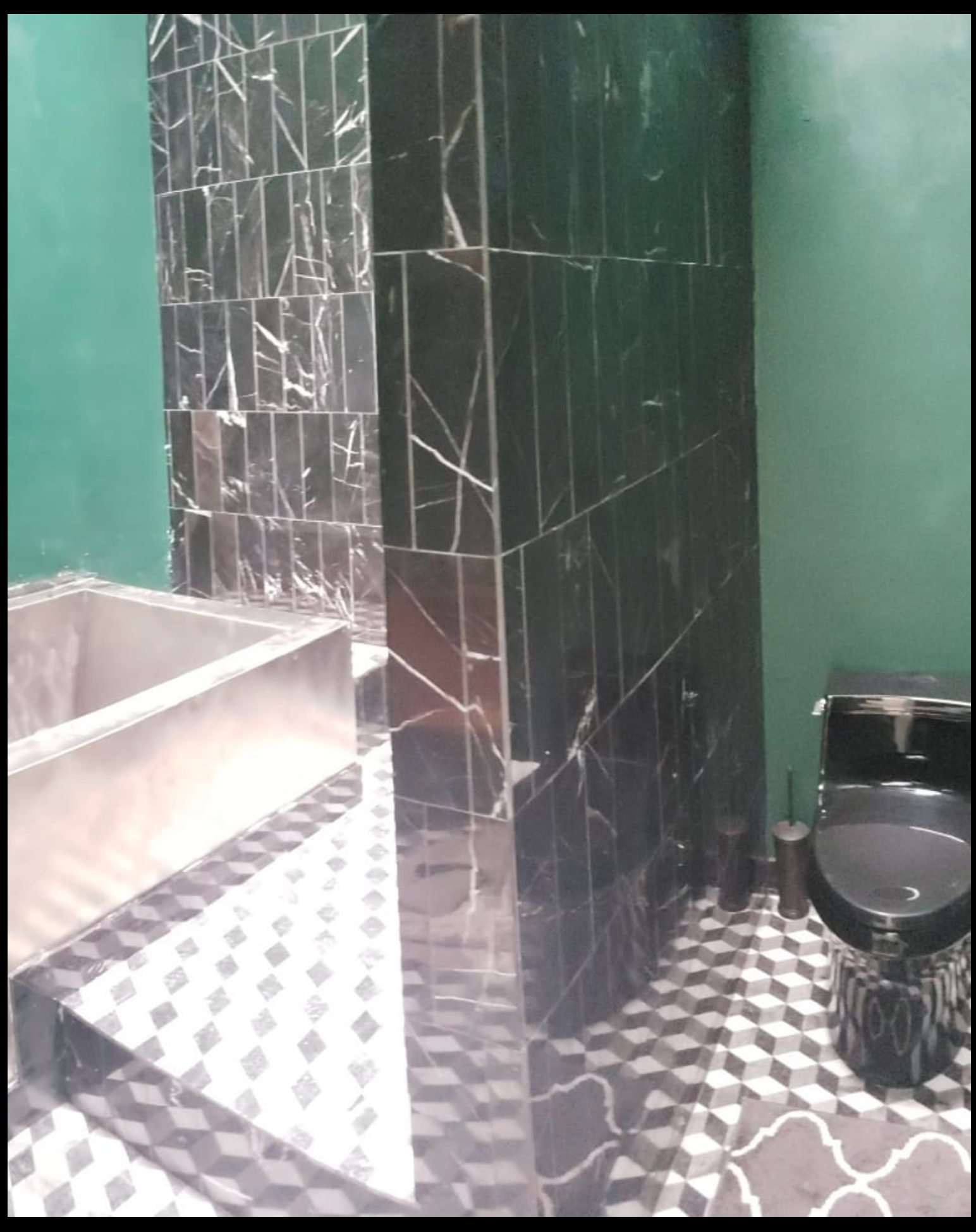 A bathroom with green walls and black and white tiles