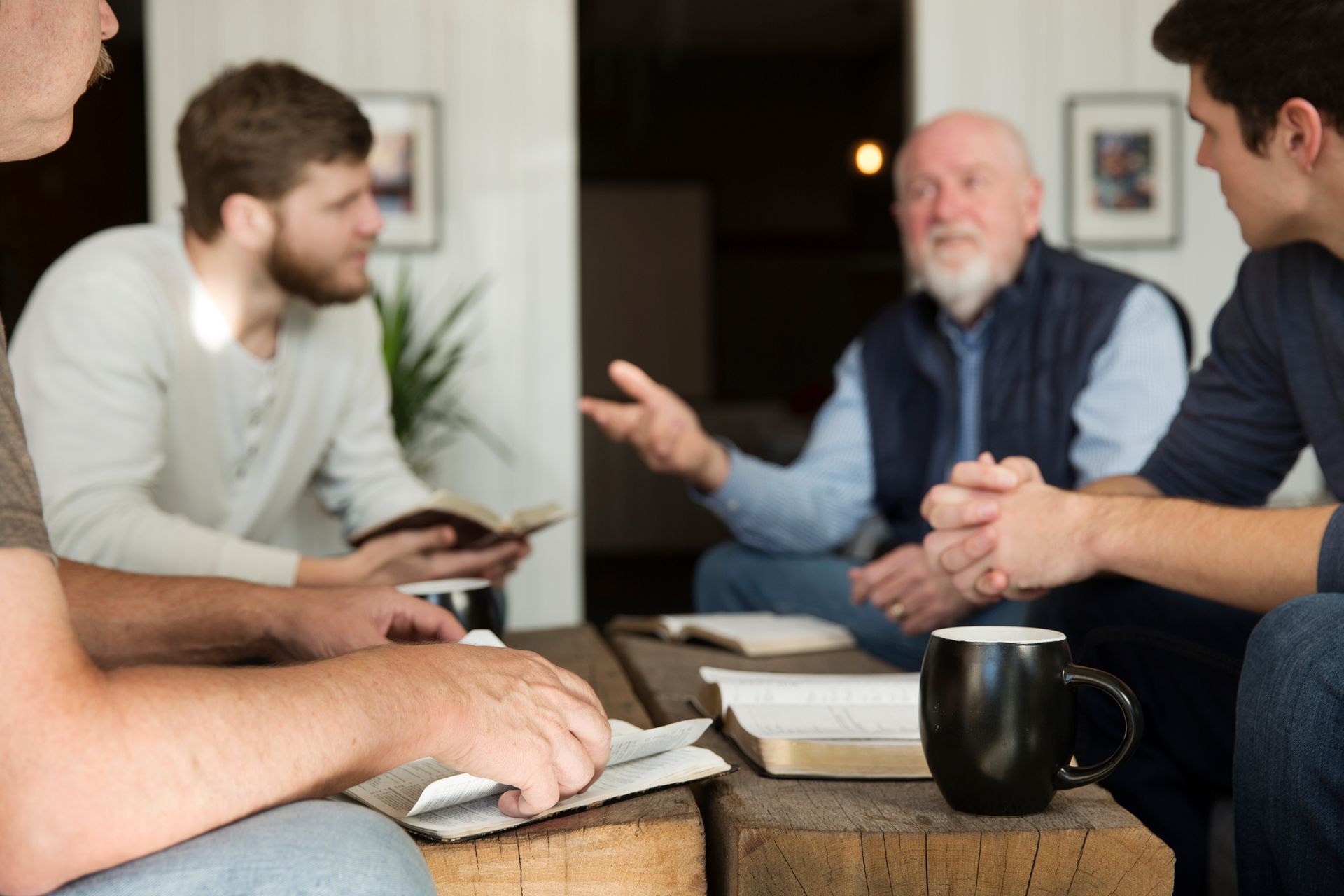 People in a living room discussing over coffee, with books and a notebook on the table