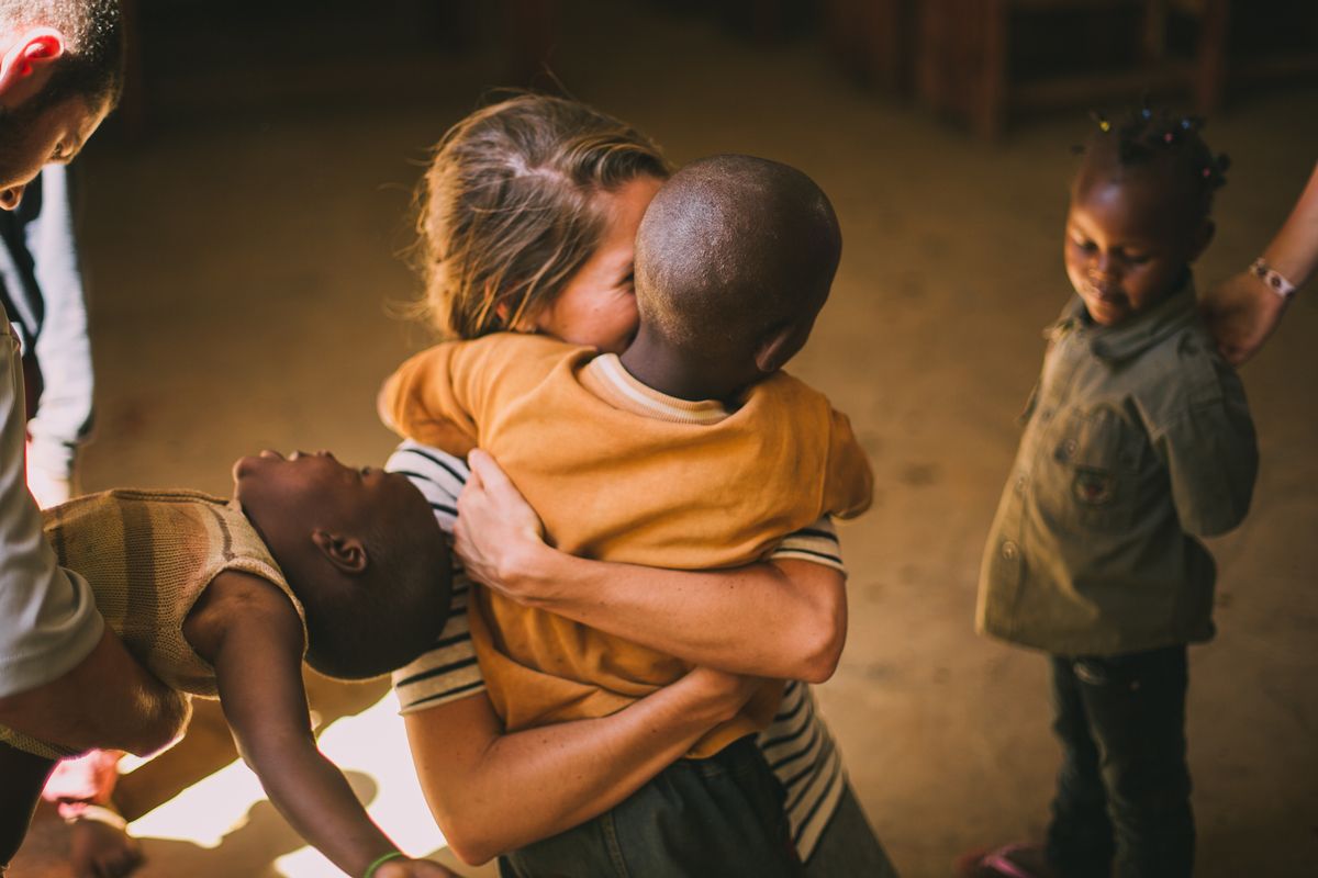 Children embracing warmly indoors, with one child holding another in a dimly lit room