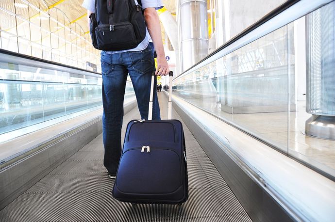 Traveler pulling a navy rolling suitcase through an airport corridor with glass railings