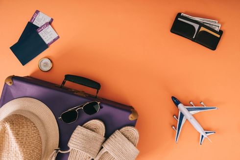 Accesorios de viaje sobre fondo naranja: maleta, sombrero, gafas de sol, sandalias, pasaporte, reloj y avión de juguete.