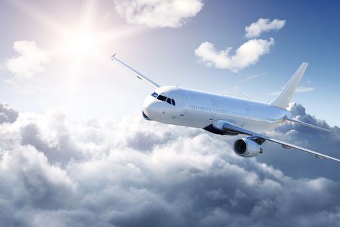 White passenger jet flying above clouds under a bright sky