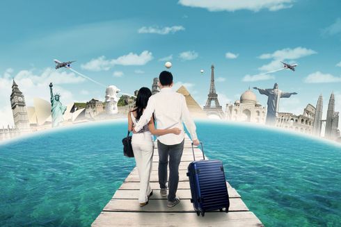 Couple walking on a pier with a suitcase toward a city skyline across turquoise water under a blue sky