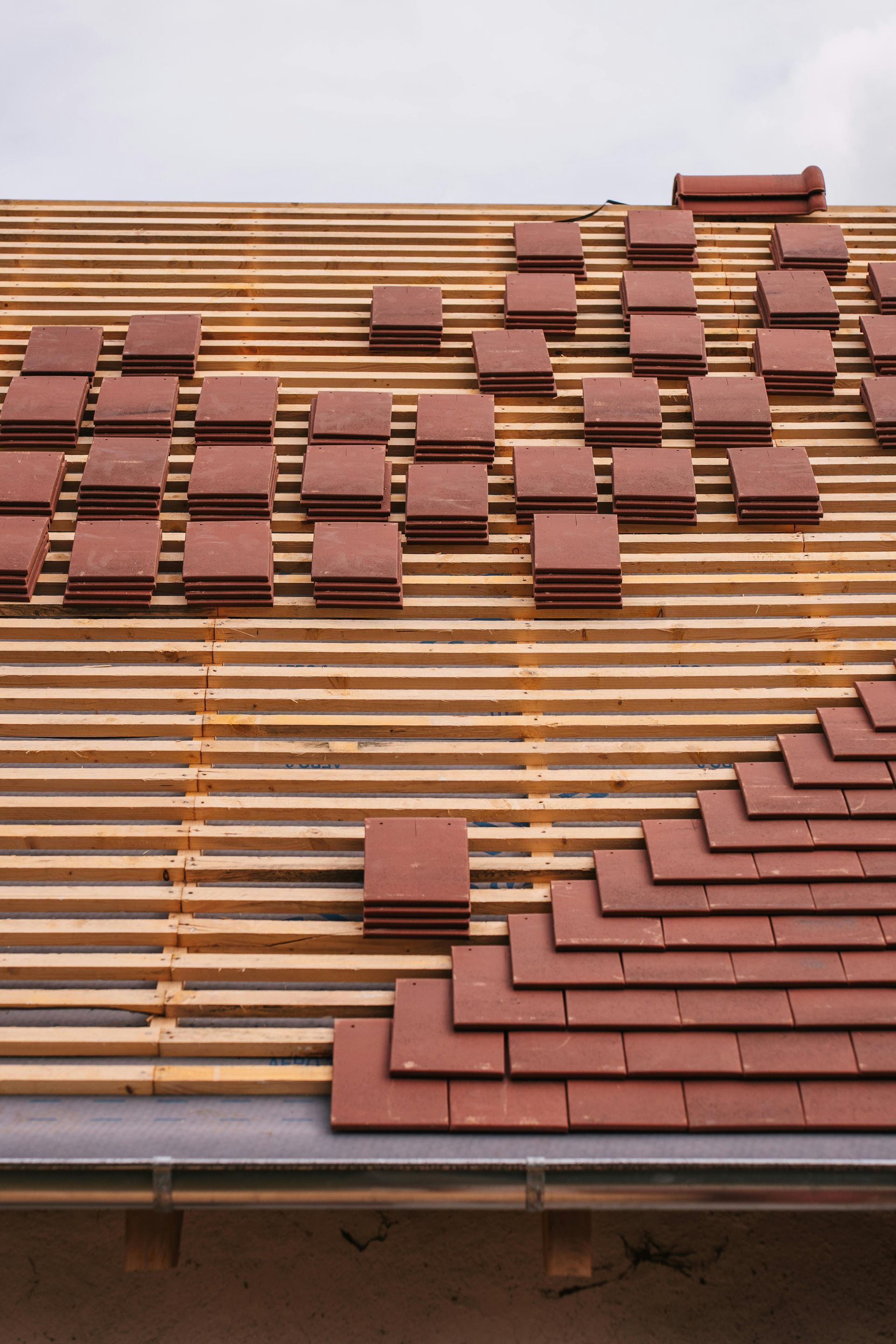 Roof under construction with red tiles partially installed on wooden framework.