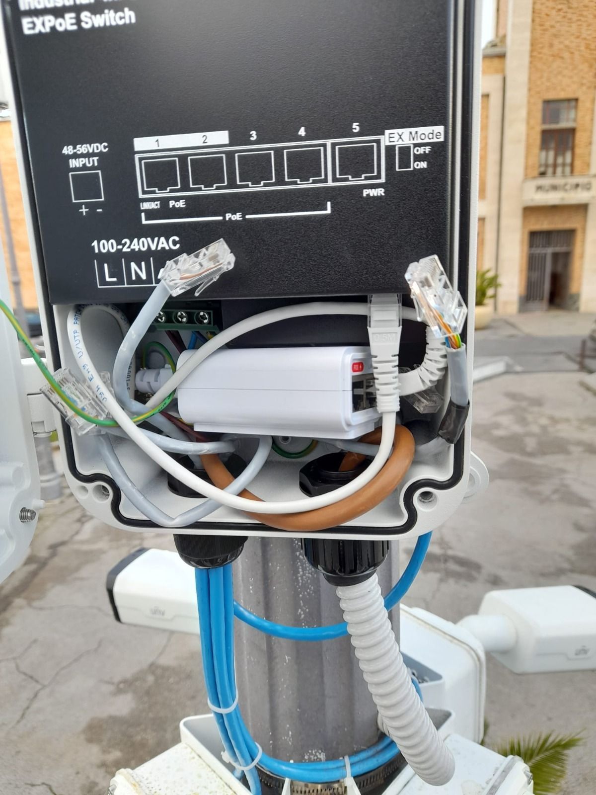 Una scatola da cui escono dei fili è posta in cima a un palo.