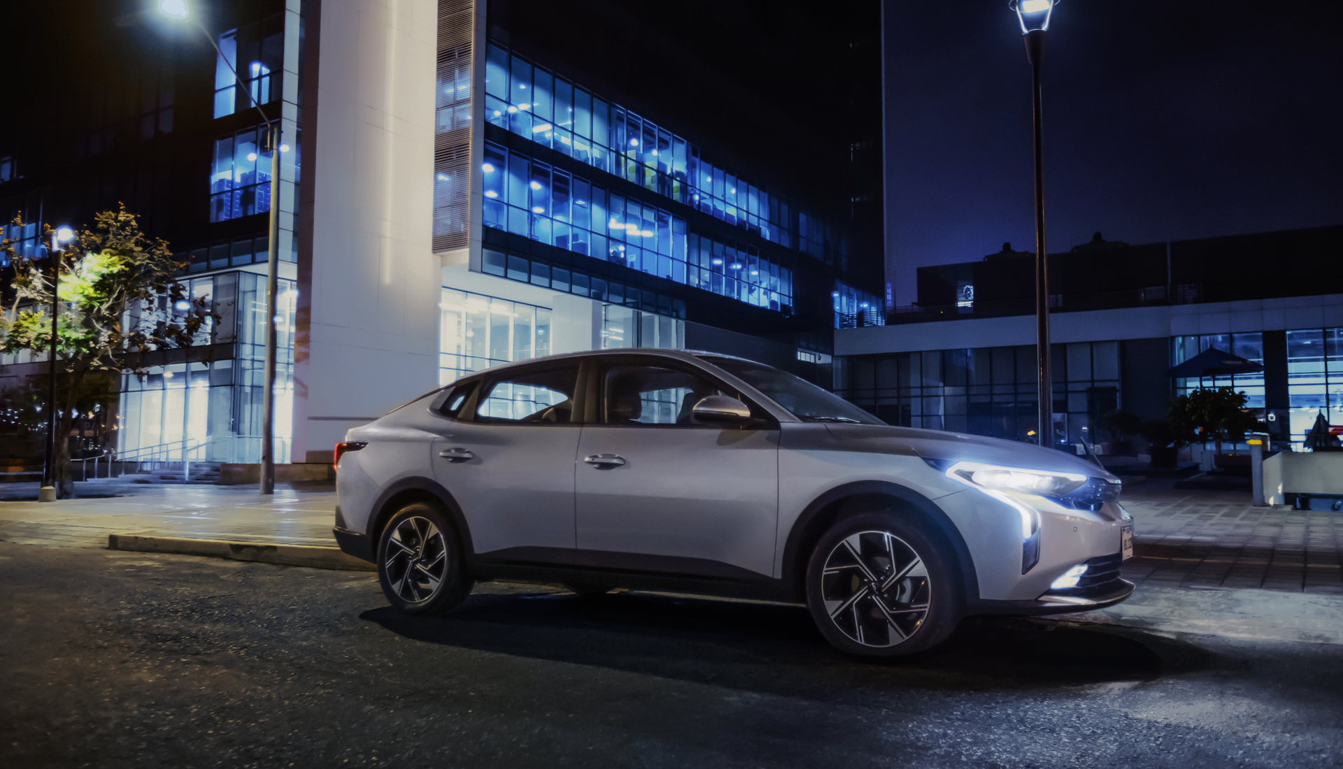 A silver car is parked in front of a building at night.