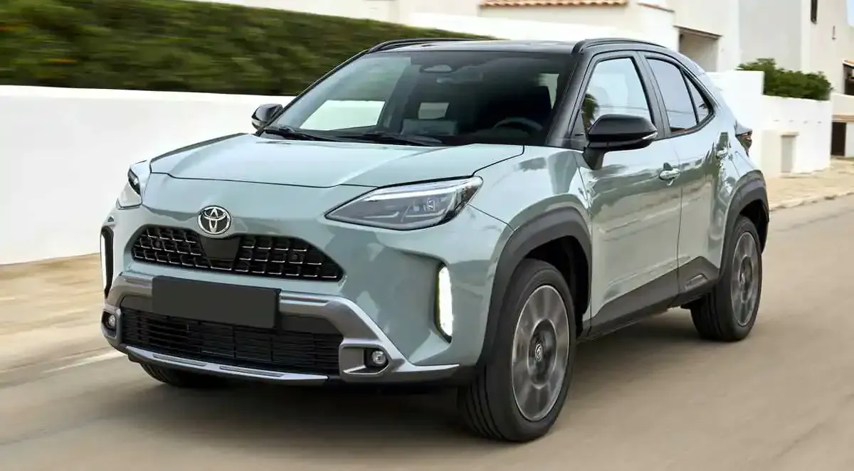 A toyota yaris cross is driving down a road next to a building.