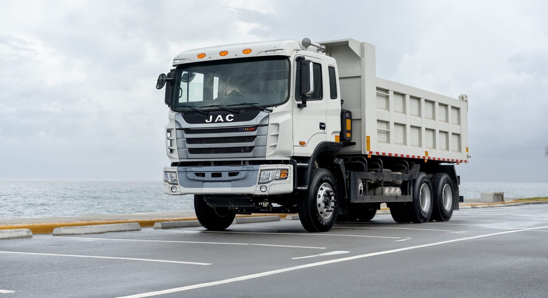 A white dump truck is driving down a road next to the ocean.