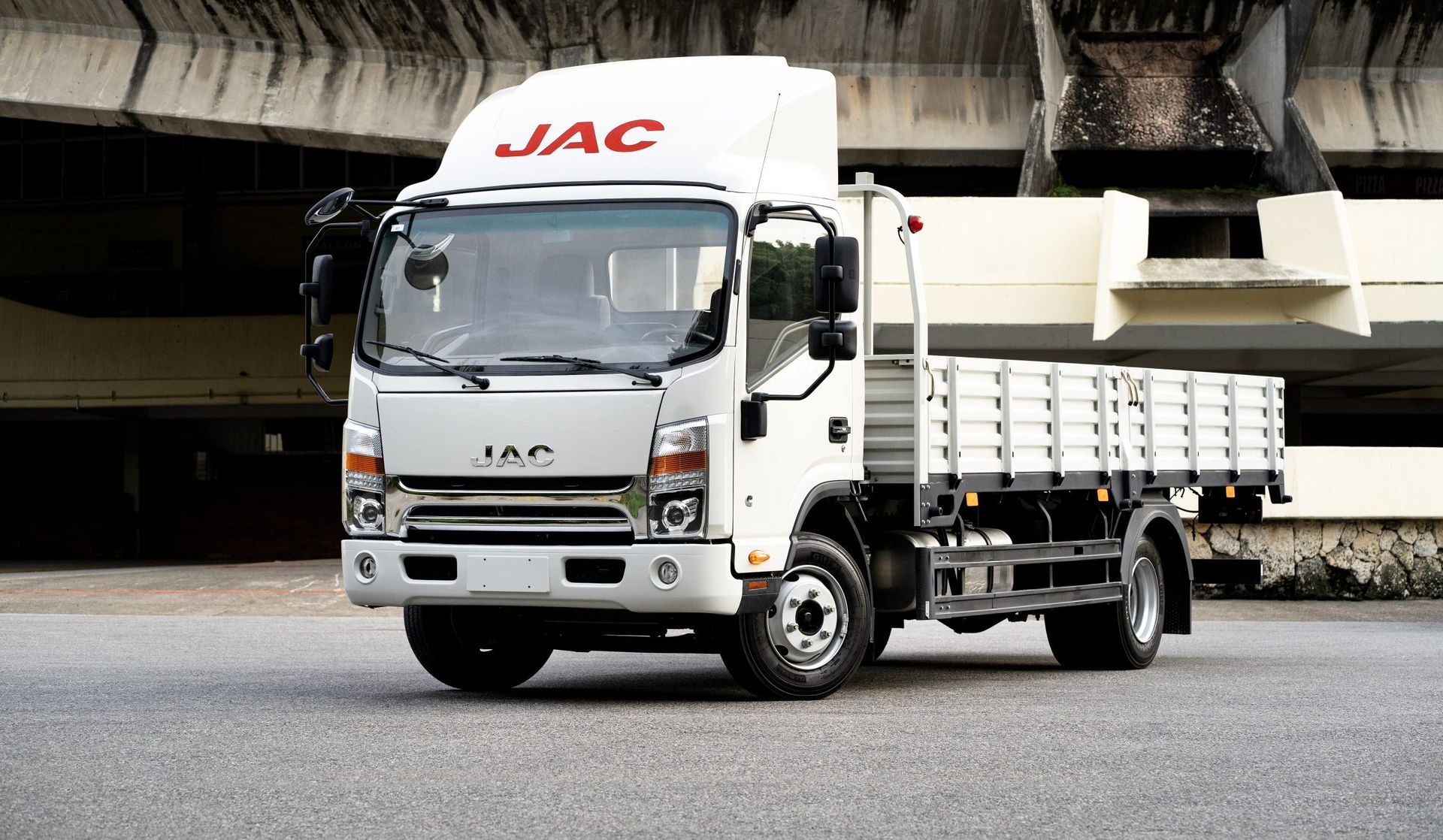 A white jac truck is parked in front of a building.