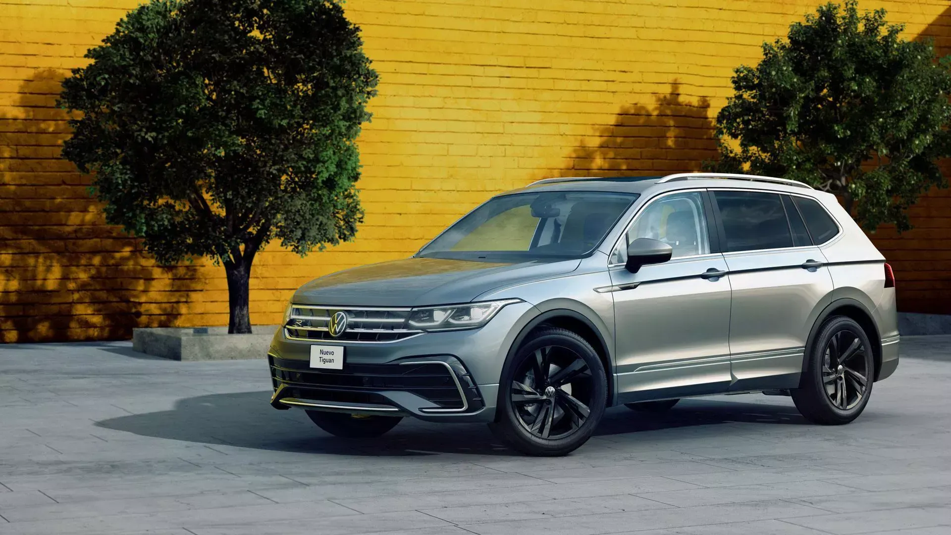 A silver volkswagen tiguan is parked in front of a yellow brick wall.