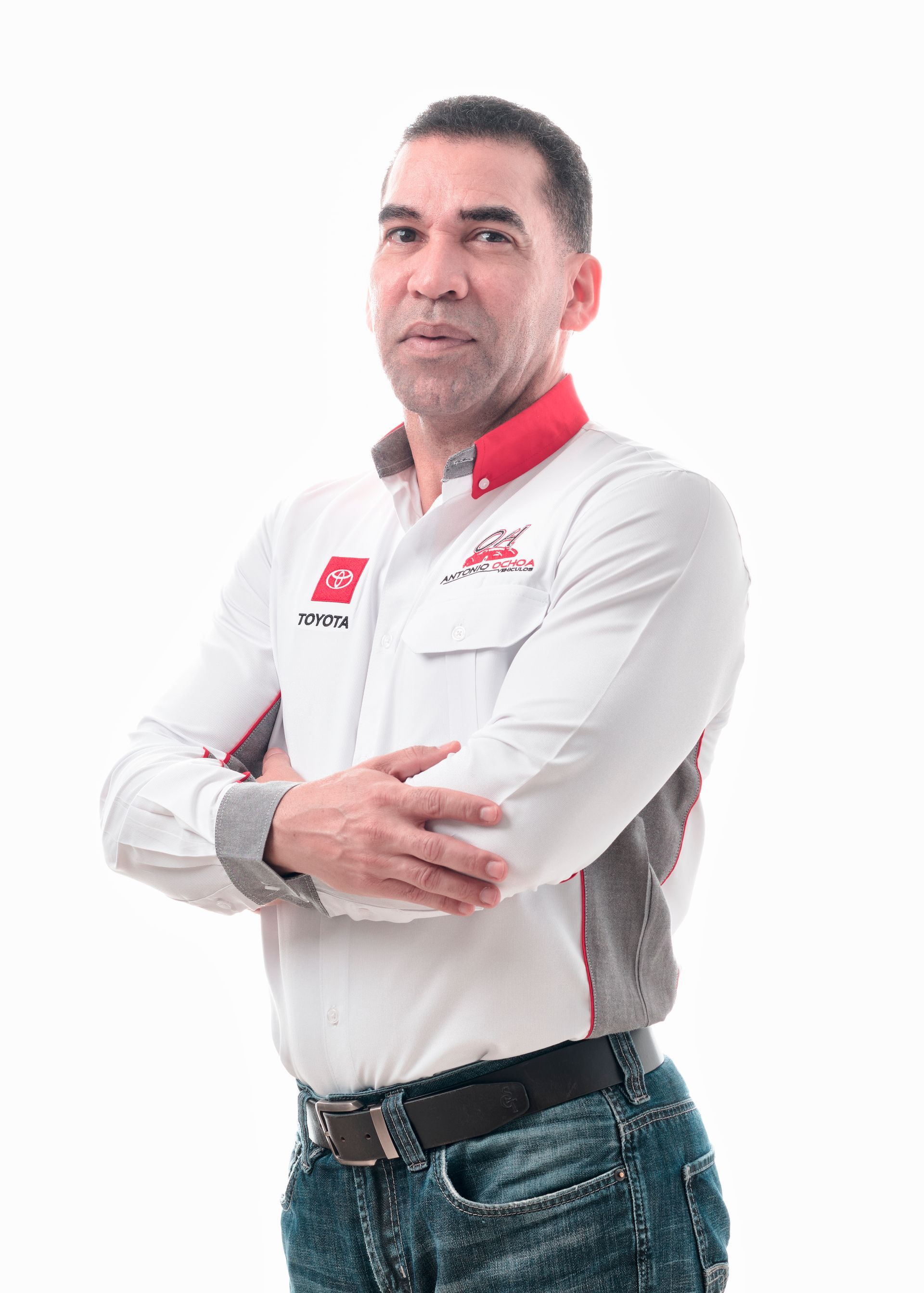 A man in a white shirt and jeans is standing with his arms crossed.