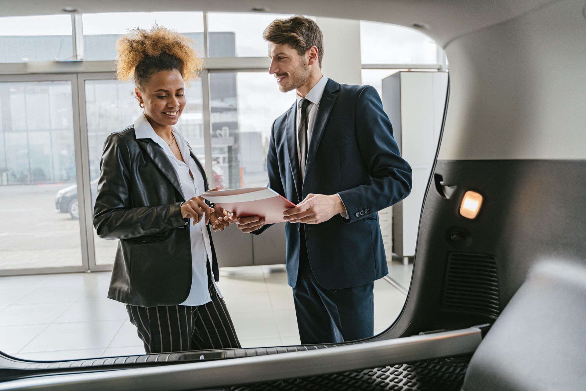 A man and a woman are looking at a car in a showroom.