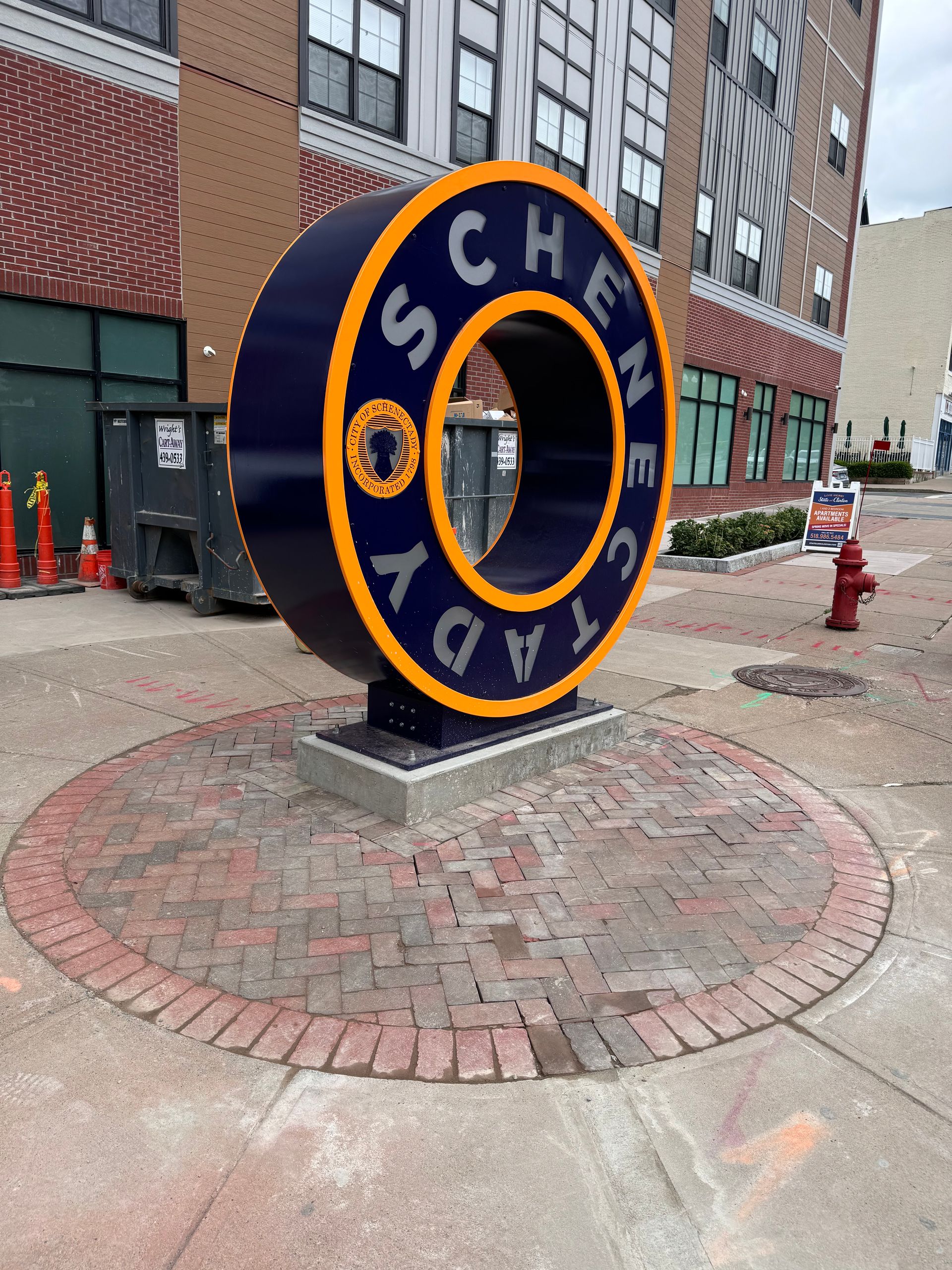 White house with a porch, three dormers, and brown roof. Blue sky, green lawn, and trees in the background.