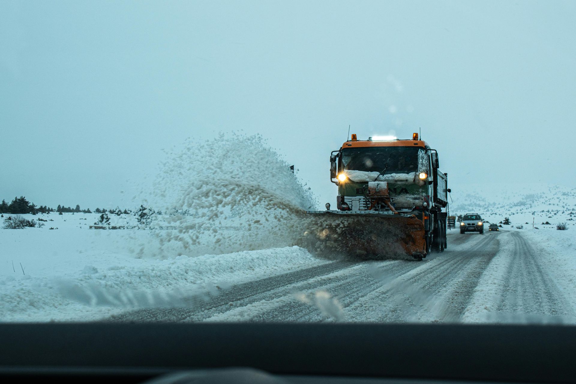 Men shoveling snow near a red snow groomer on a snowy slope.
