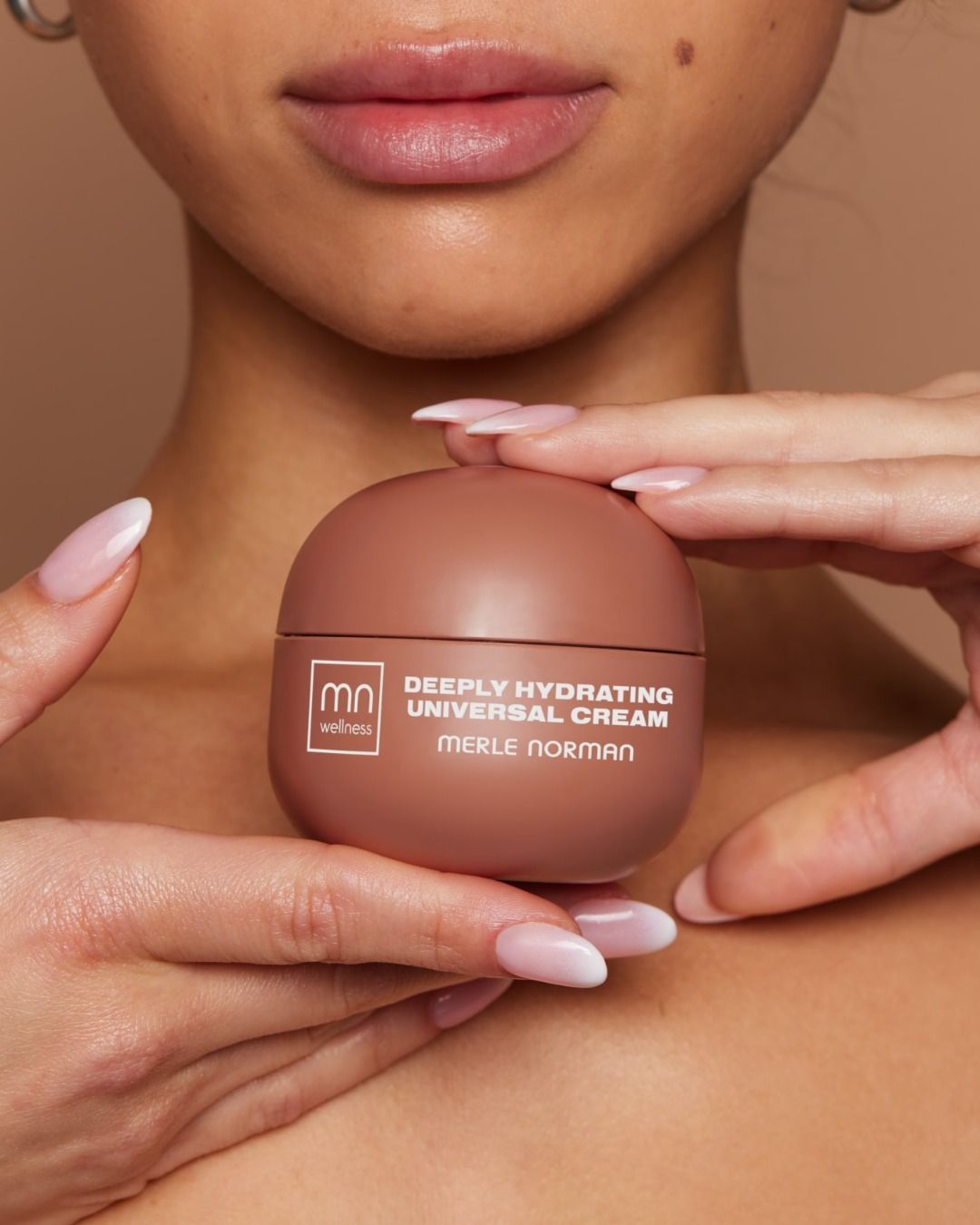 Woman holding a brown skincare cream jar, the label reads 