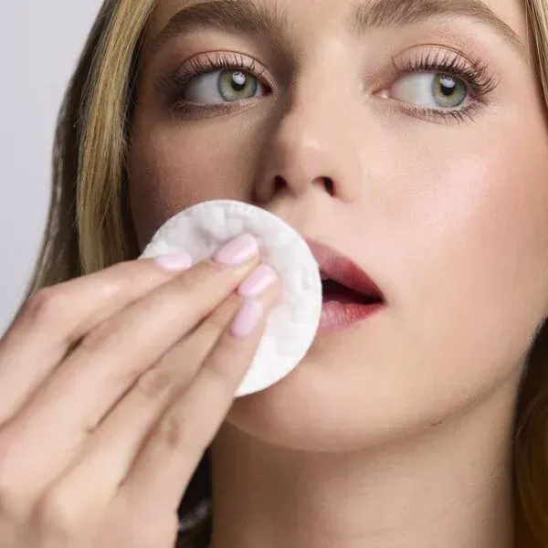 Woman holding cotton pad to lips, removing makeup.
