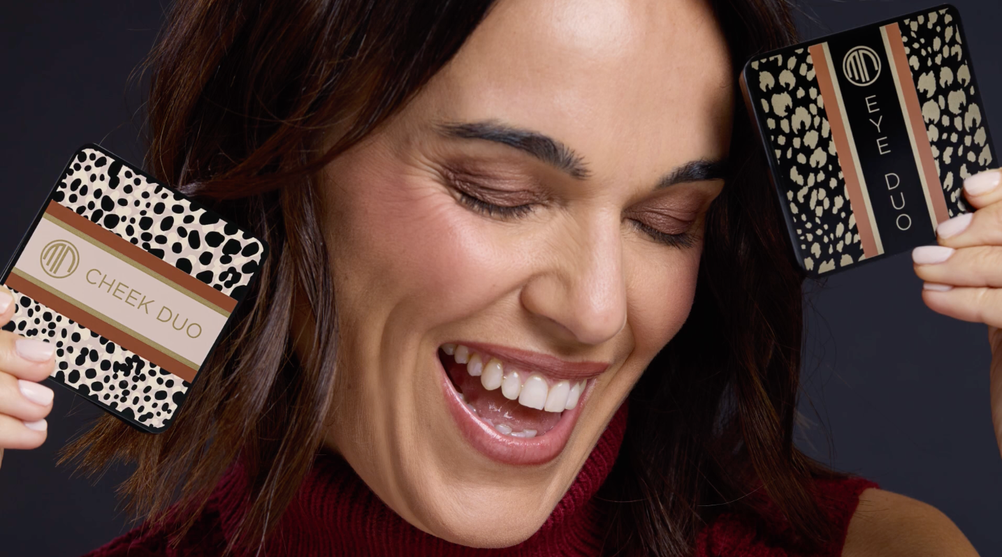 Woman smiling, holding two makeup compacts with animal print design.
