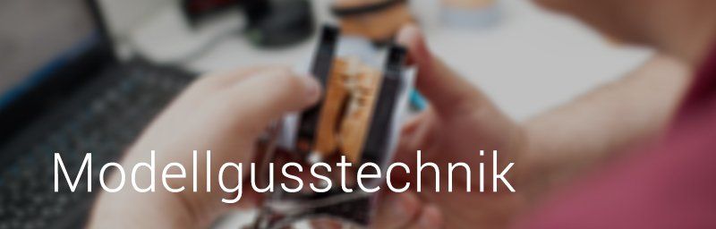 Hände halten ein Zahnmodell mit dem darüber gelegten Text „Modellgusstechnik“.