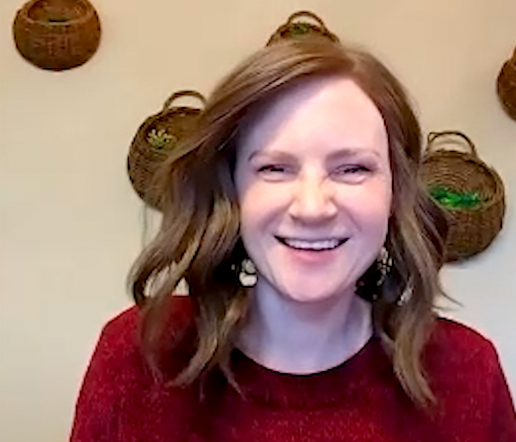 A woman is smiling in front of a wall with baskets on it.