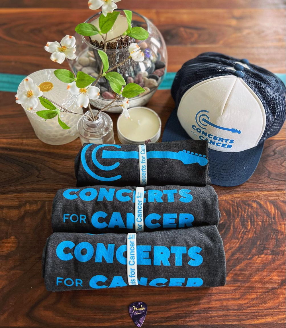 A stack of concerts for cancer shirts on a wooden table