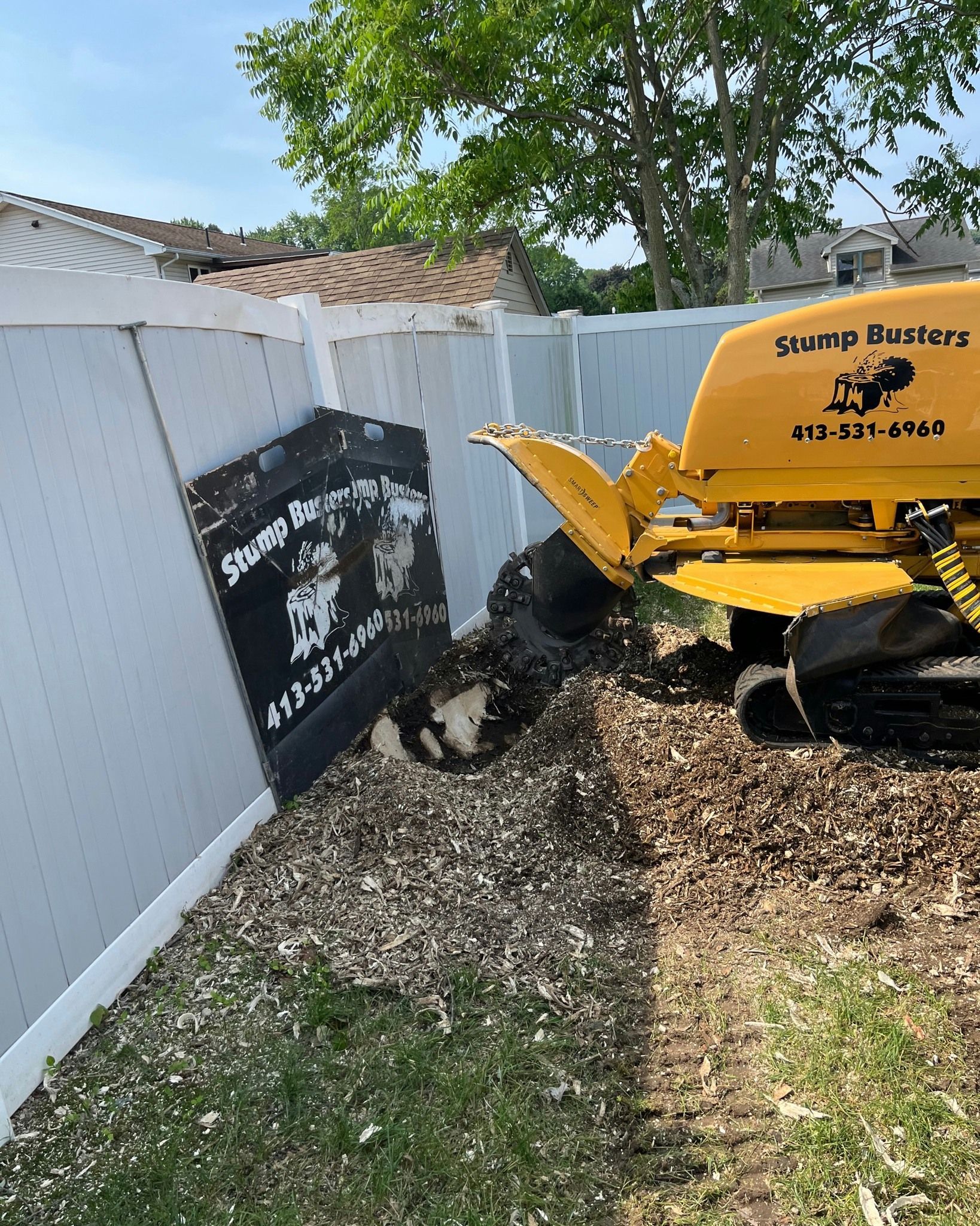 Yellow stump grinder removing a tree stump next to a white fence.