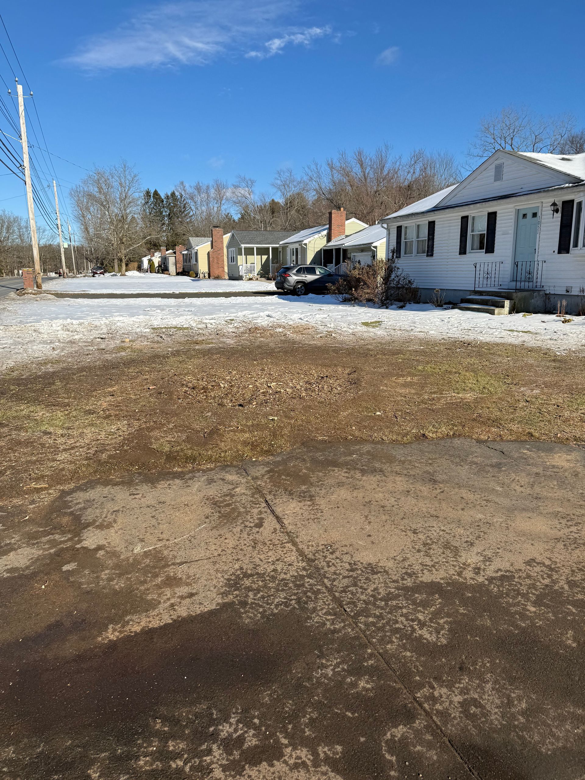 Houses on a street covered in patchy snow, with a clear blue sky above.