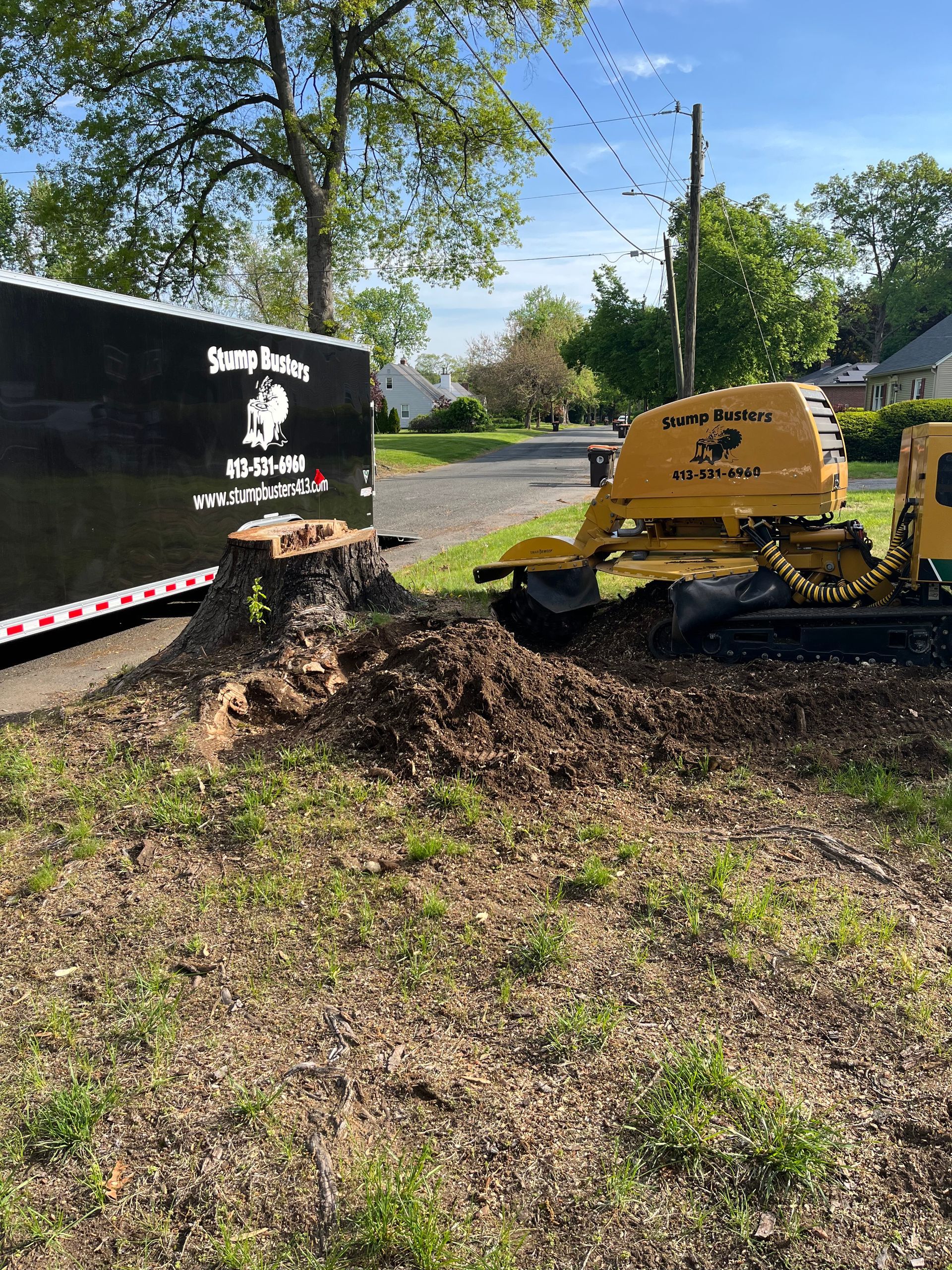 Yellow stump grinder next to a freshly ground stump and trailer, possibly a tree service.