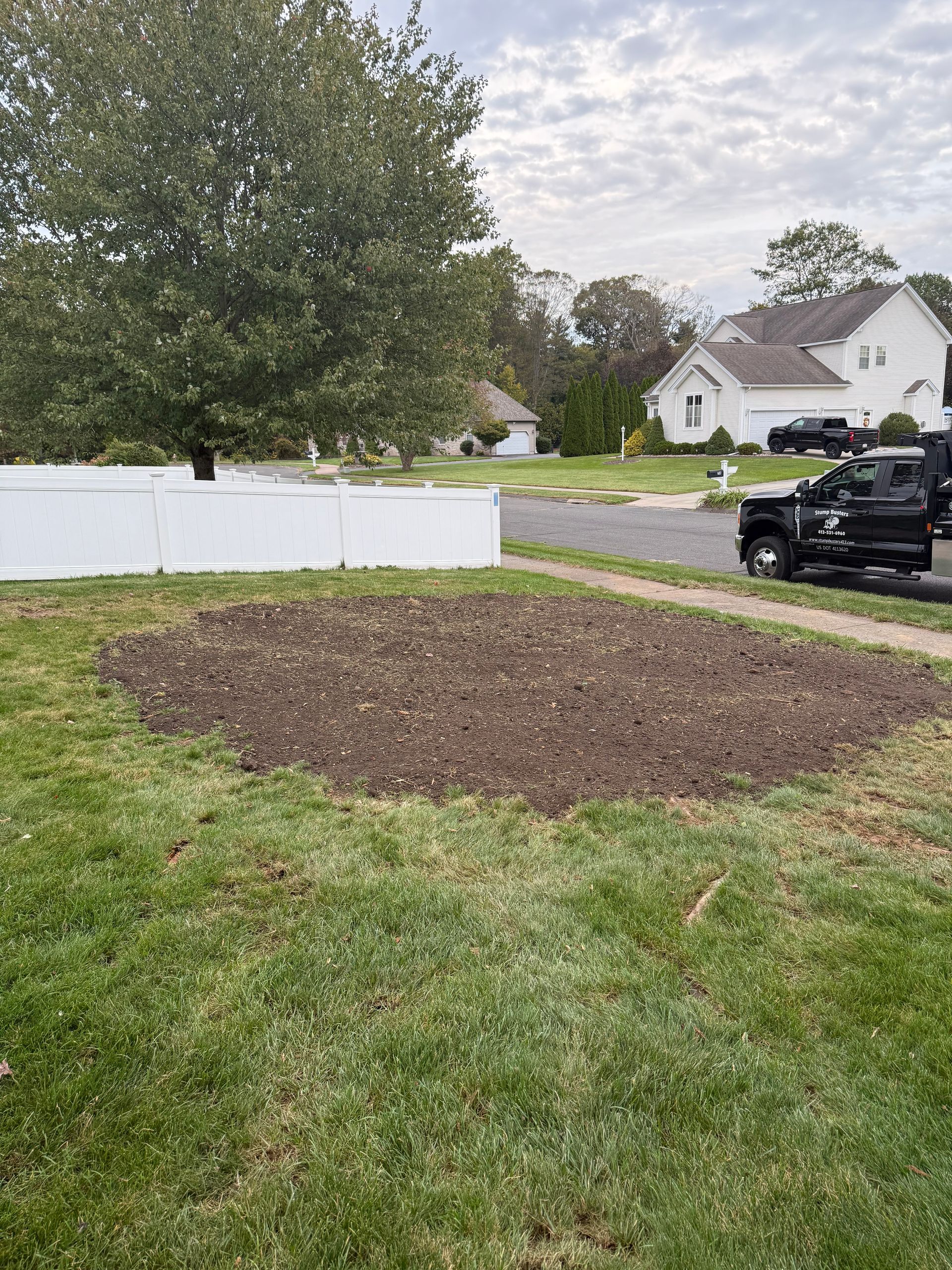 Brown earth patch in front yard, surrounded by green grass and a white fence. A black truck is parked nearby.