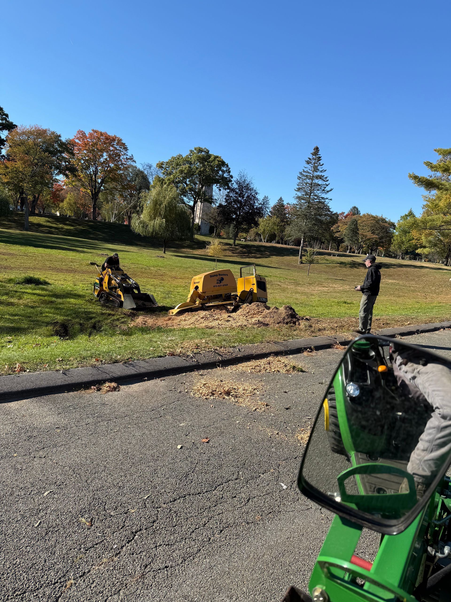 A tree stump is being ground down with a stump grinder on a grassy hill; blue sky.