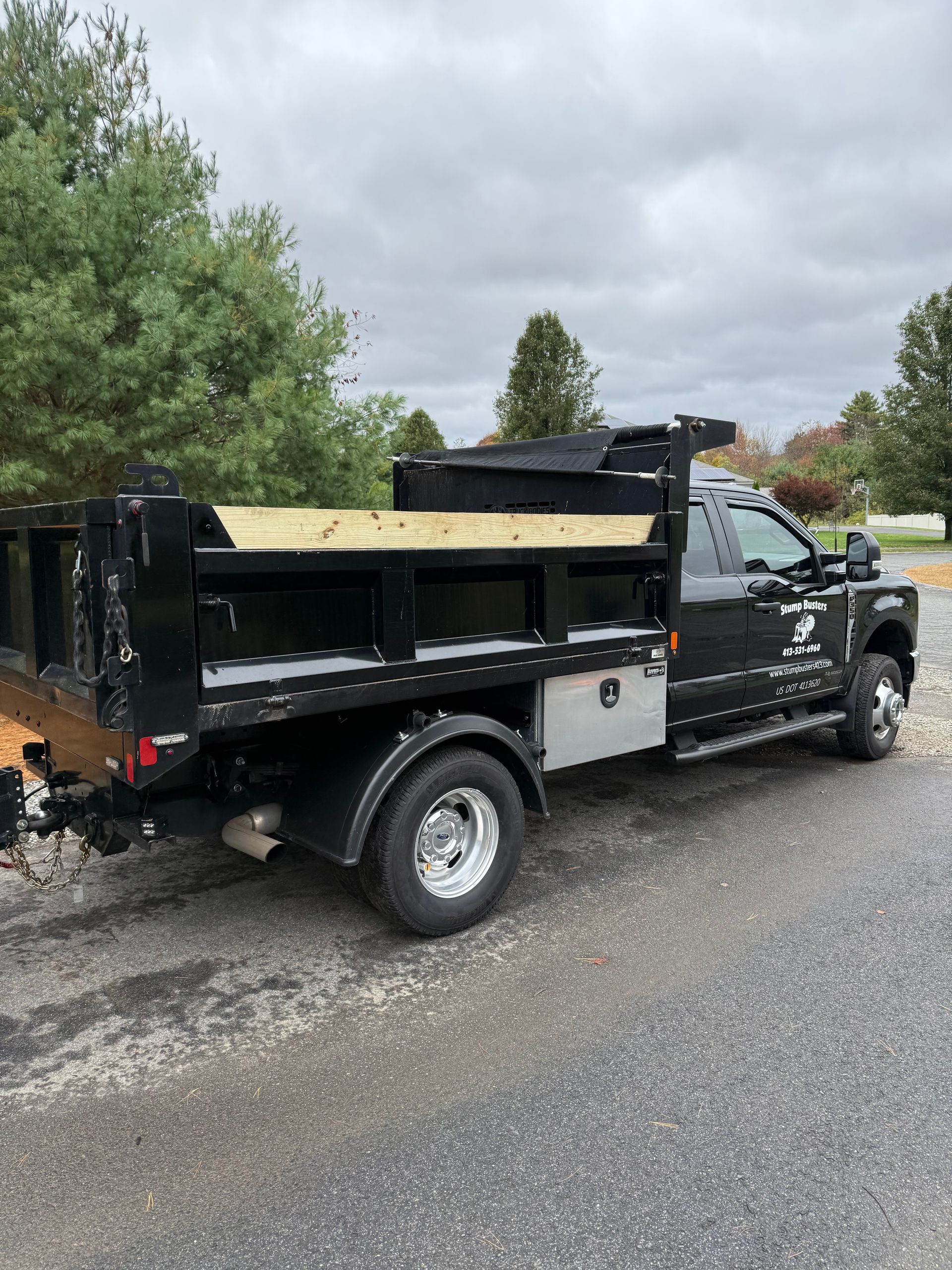 Black dump truck parked on a driveway, with a cloudy sky in the background.