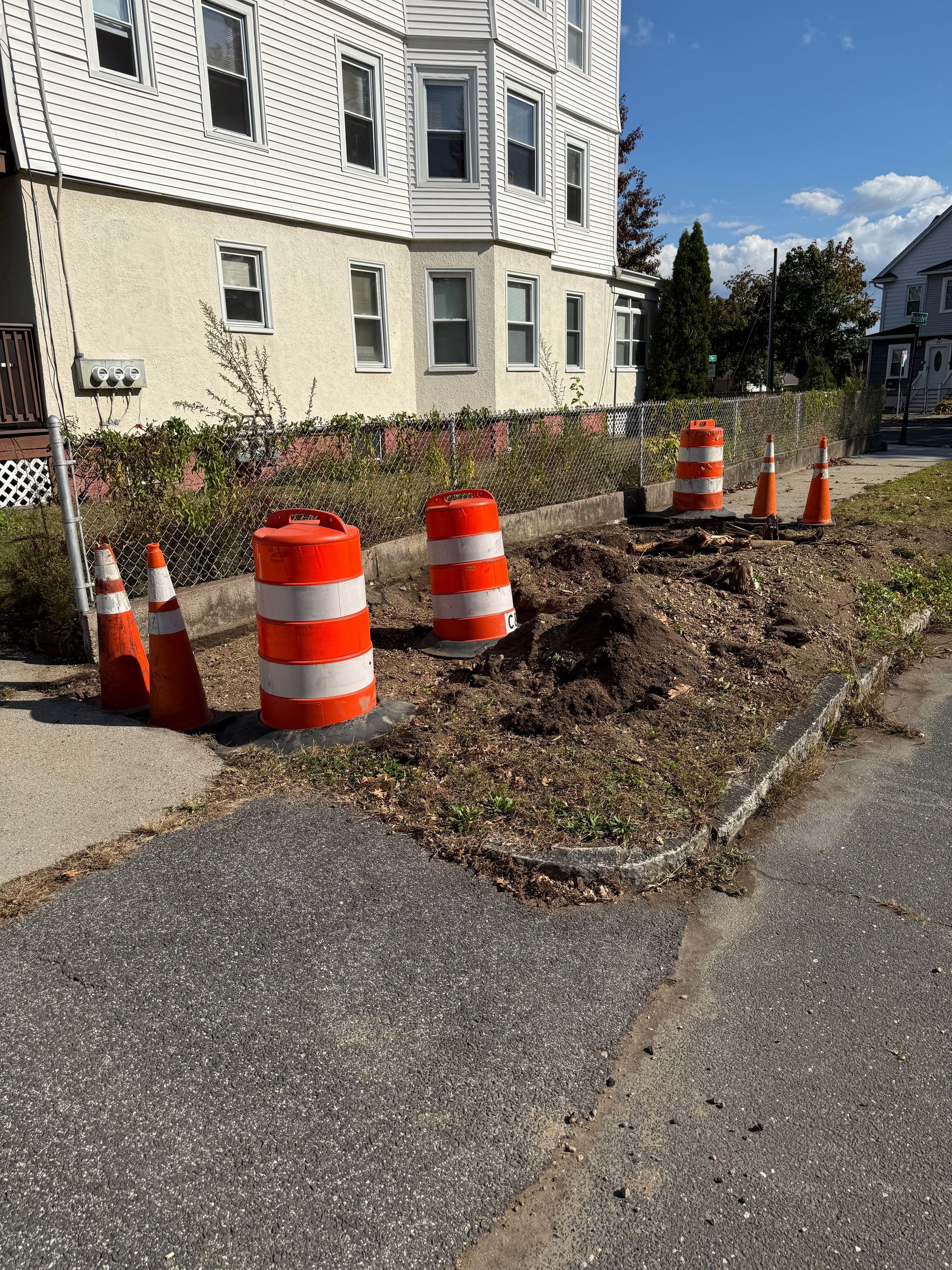 A sidewalk blocked by orange and white traffic barrels and cones. Construction in progress next to a building.
