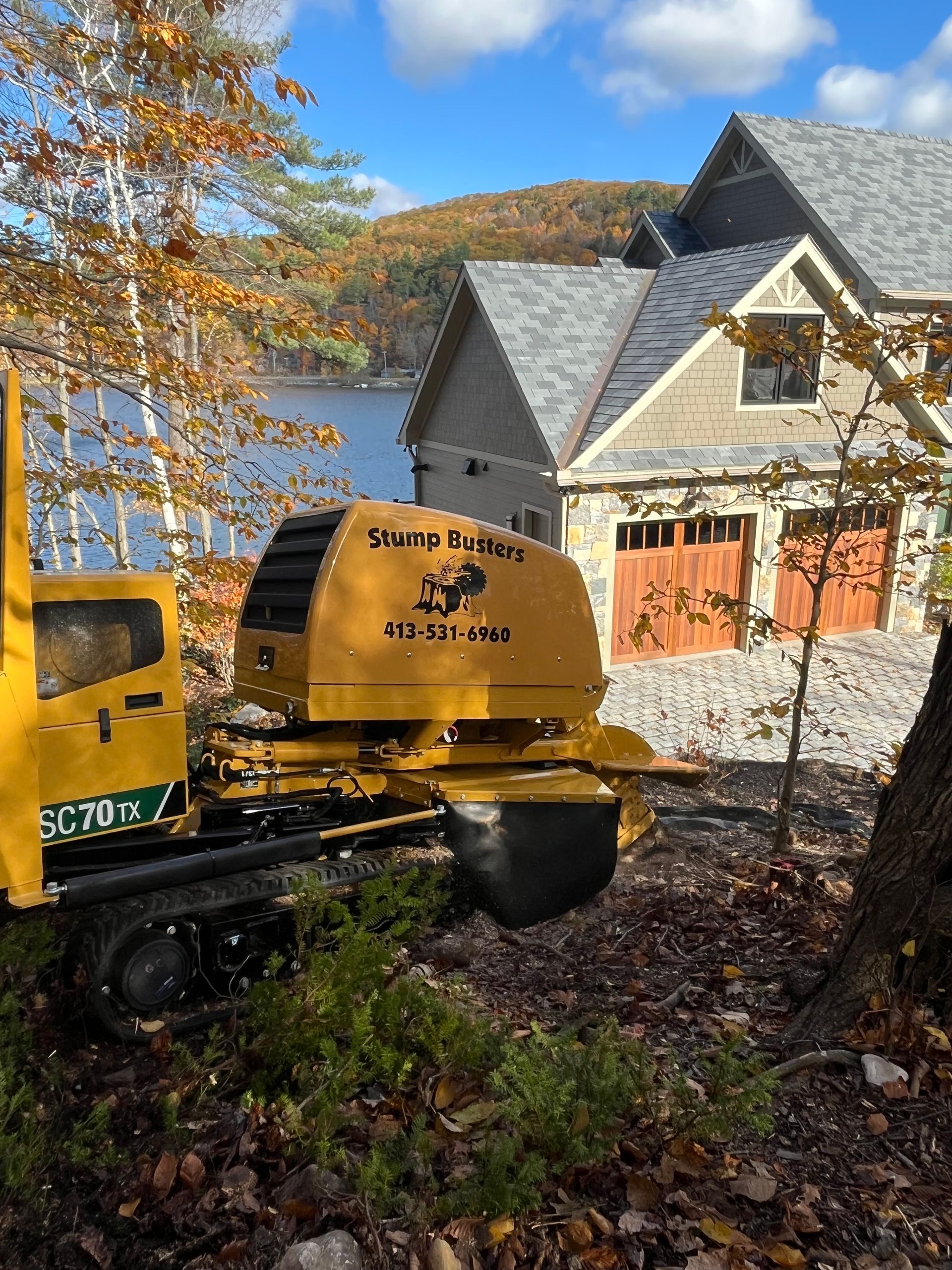 Yellow stump grinder near a house by a lake.