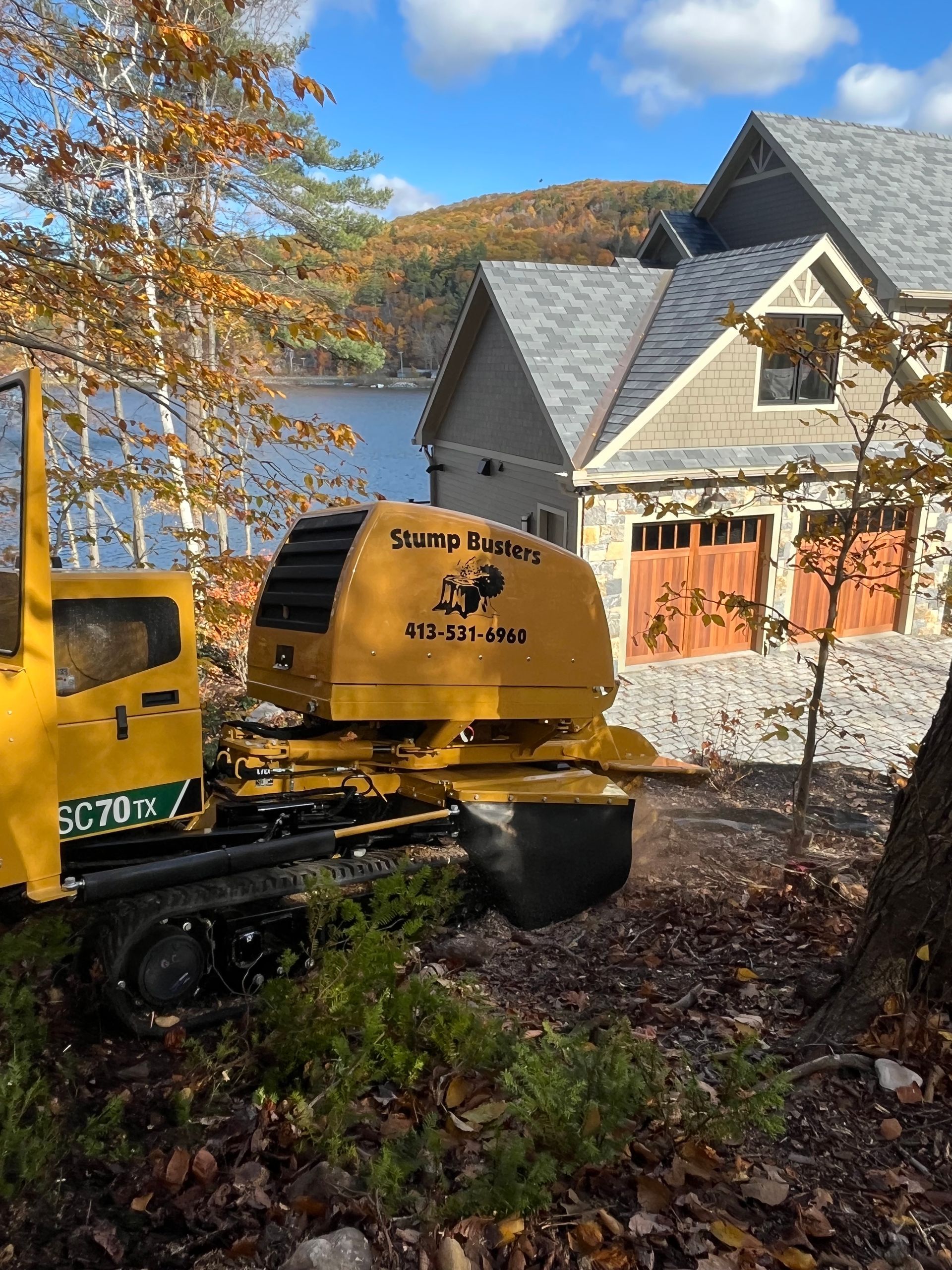 Yellow drilling machine near a house with a lake in the background. 