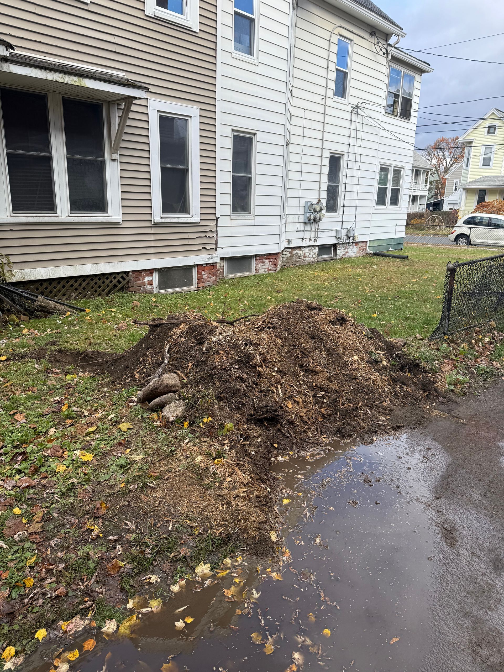 Pile of mulch and leaves on a lawn next to a two-story house with gray siding.