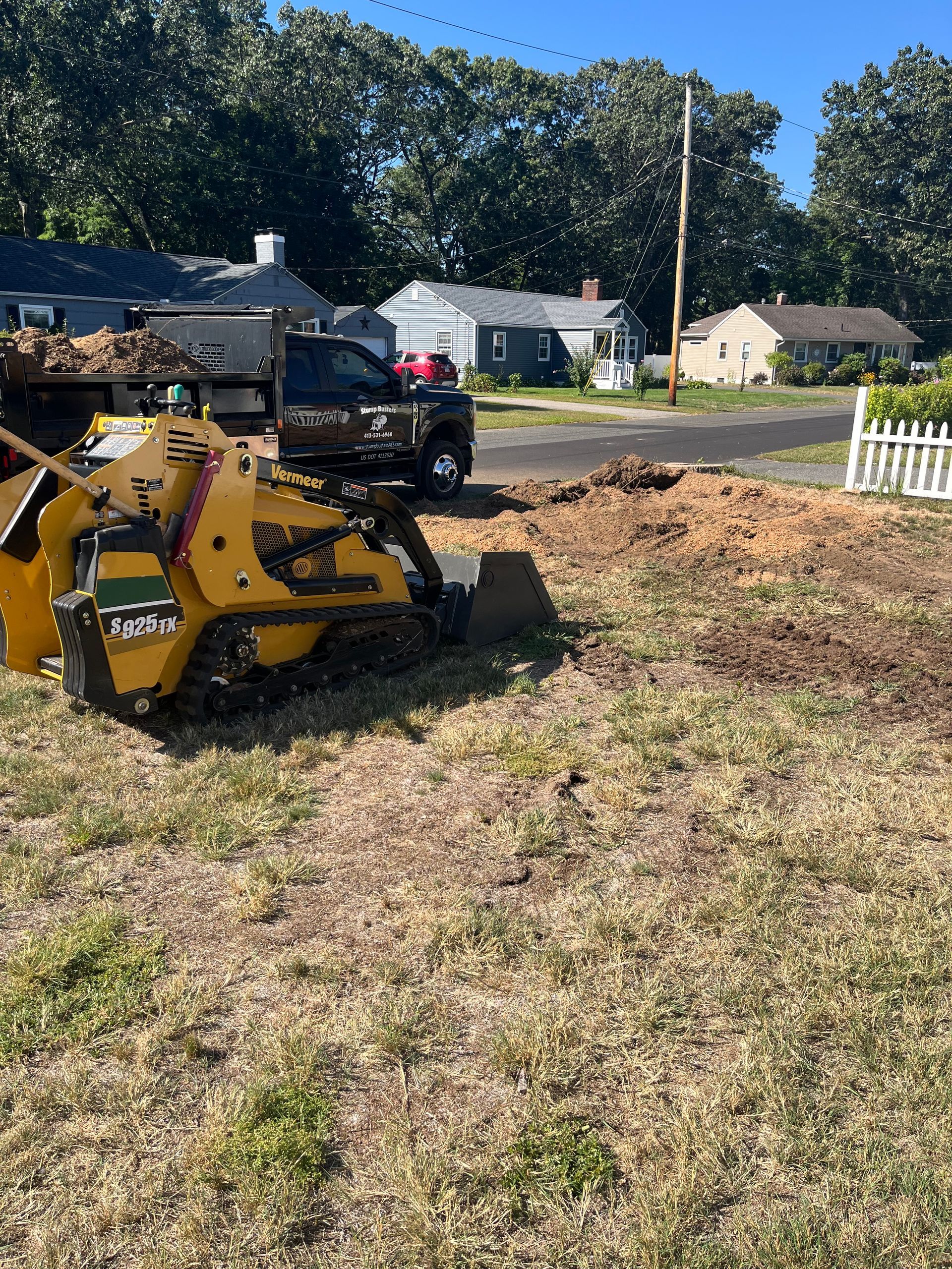 Yellow stump grinder on grass, truck in the background, residential setting.