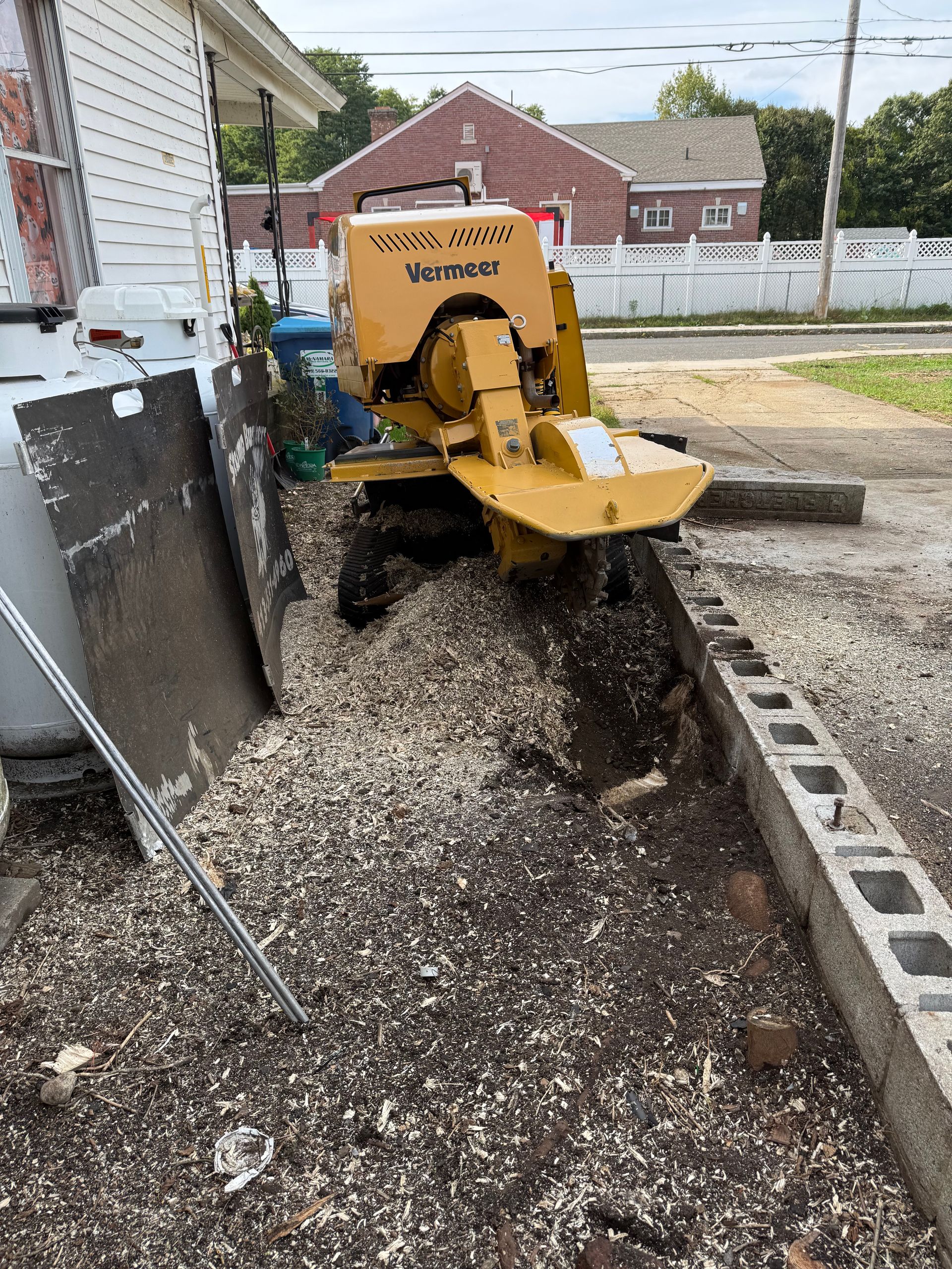 Yellow stump grinder, wood chips, concrete wall, residential setting.