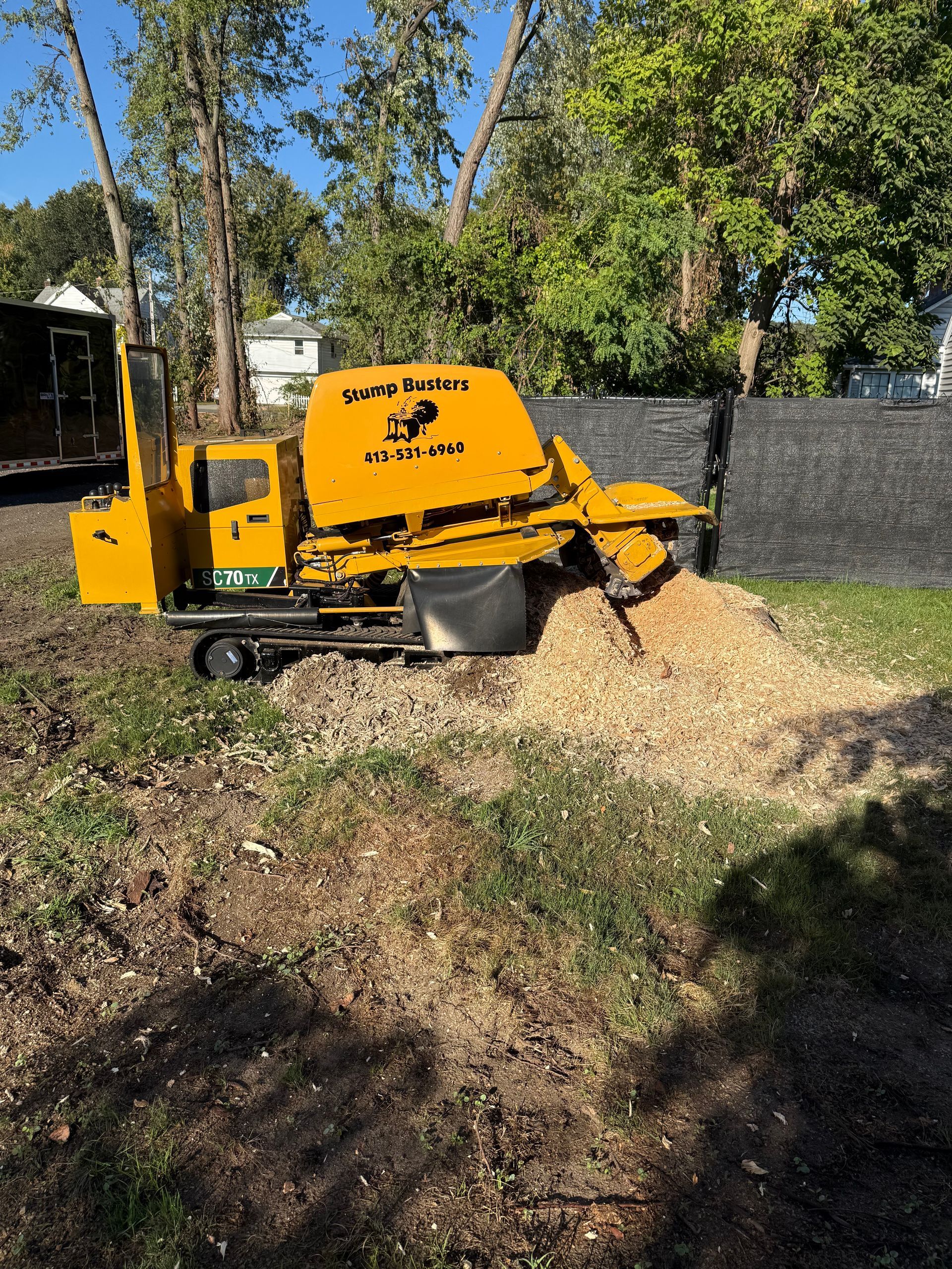 Yellow wood chipper shredding wood chips in a backyard.
