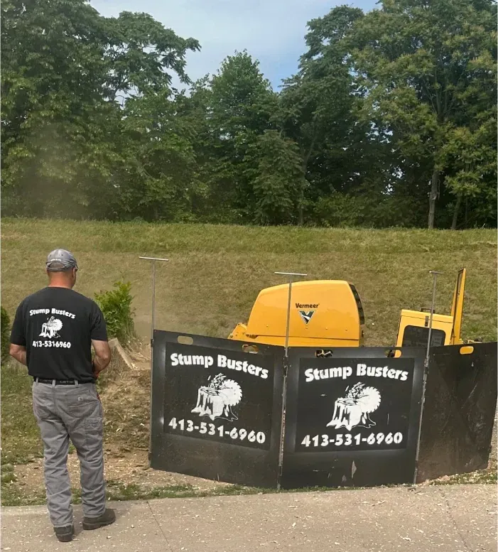 A person operates a stump grinder, surrounded by protective barriers. The machine is yellow, with the company name, 