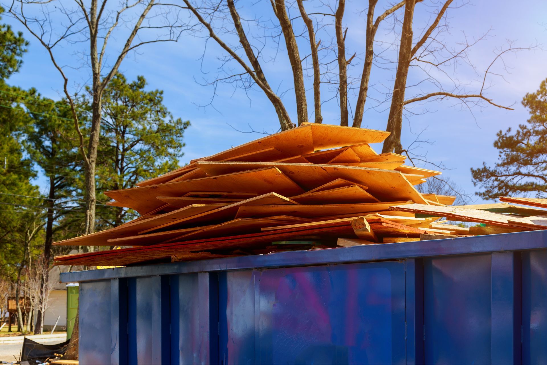 Pile of wooden boards overflowing a blue dumpster outdoors.