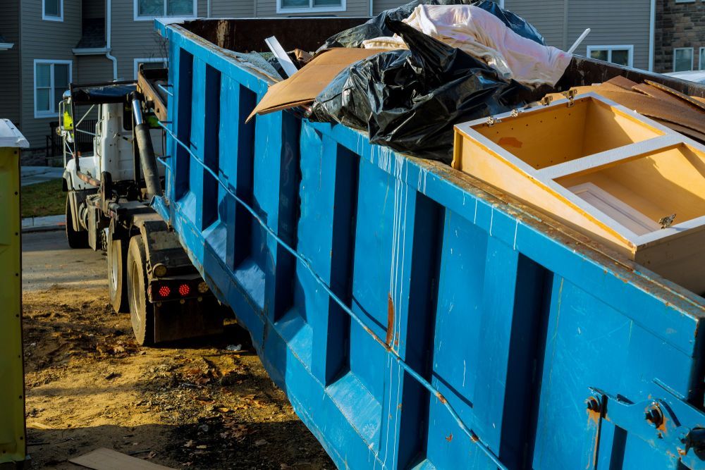 Blue dumpster filled with trash being emptied by a truck in a residential area.