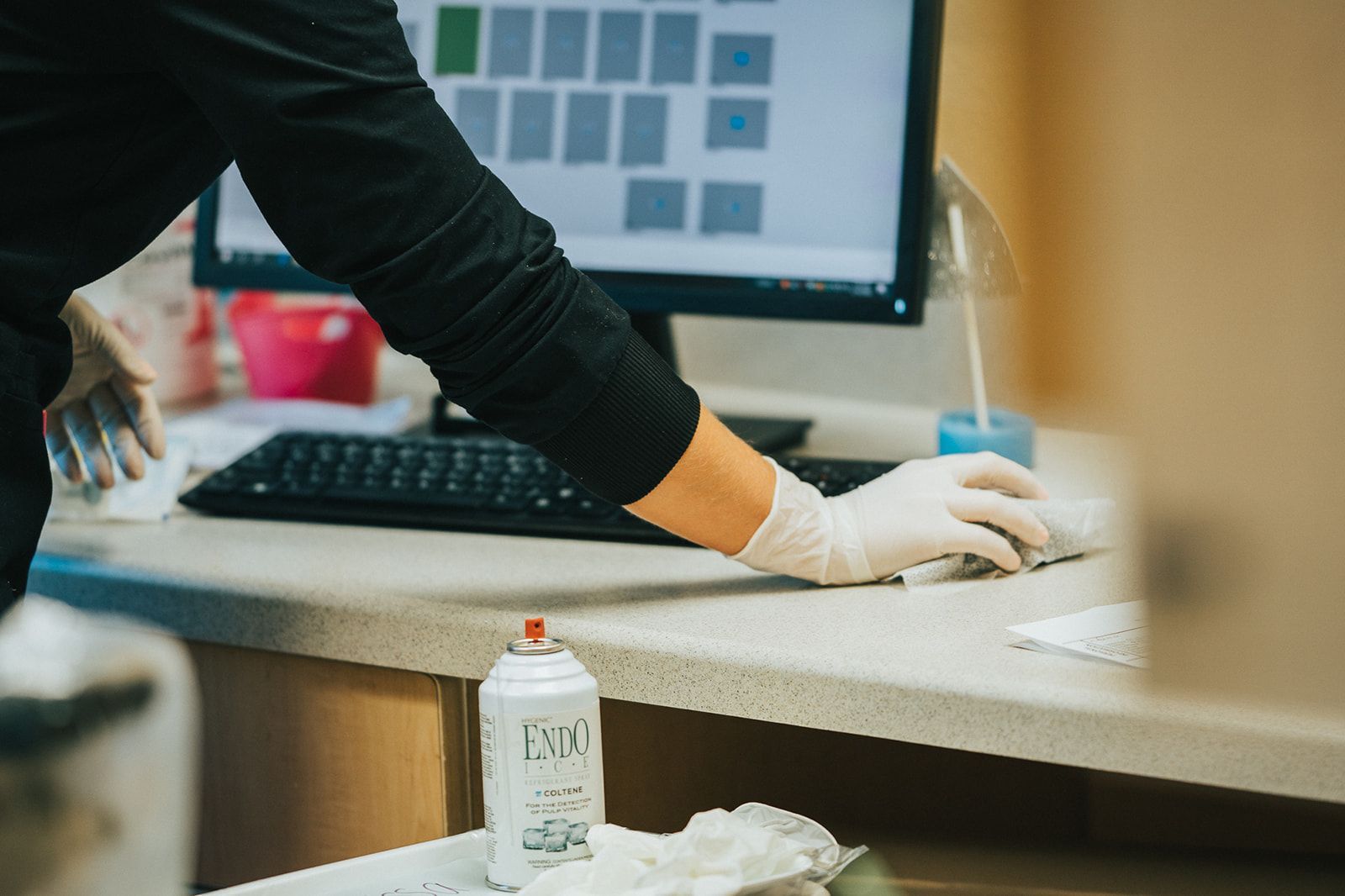 Person wearing gloves using a computer at a desk. Spray bottle and keyboard visible.