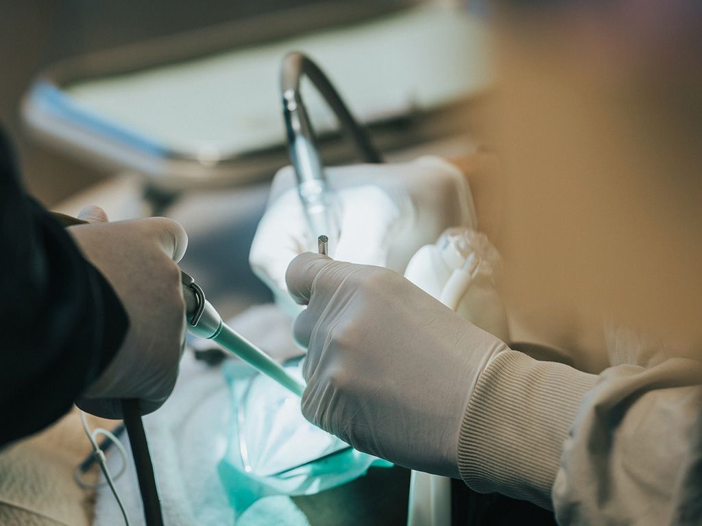 Dentist working on a patient's mouth with tools in a clinical setting.
