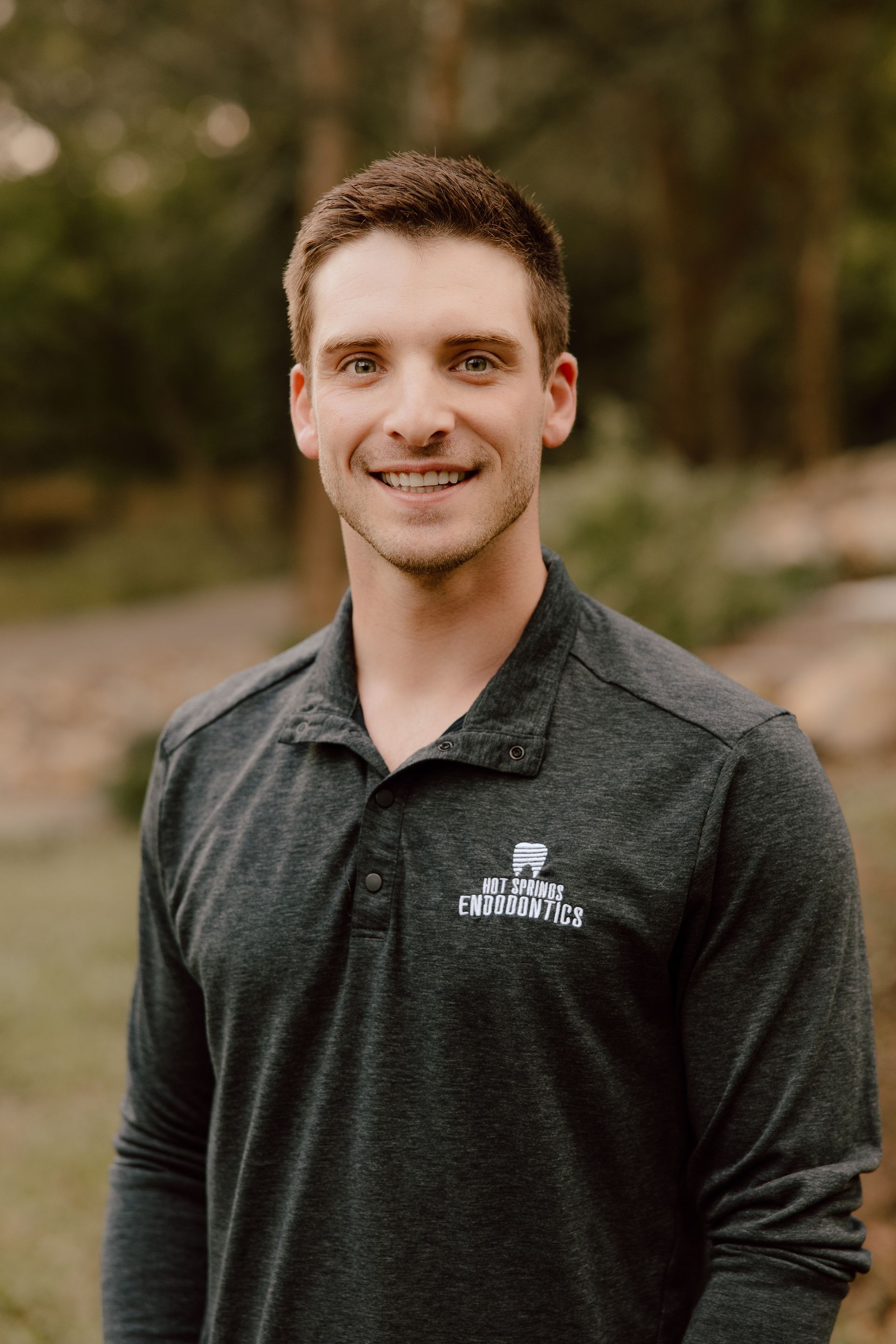 Man in gray shirt smiling outdoors.